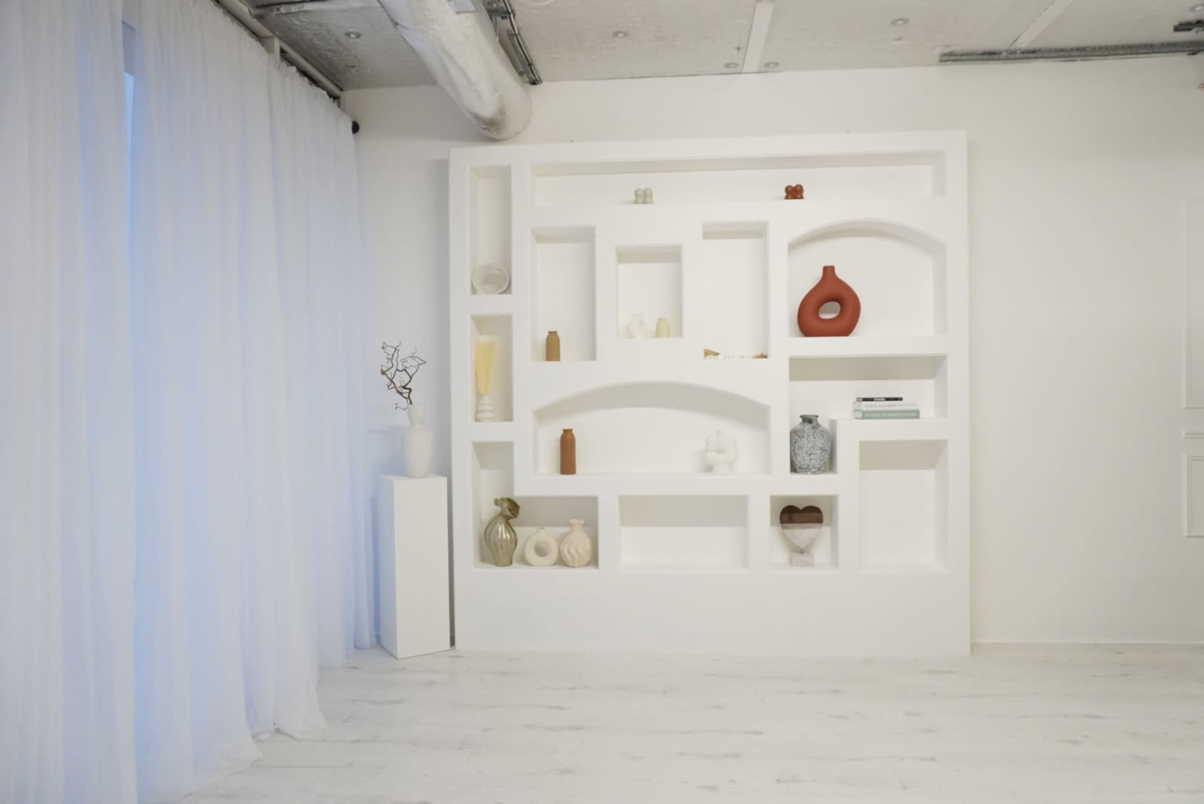 The image shows a white wall with a built-in shelving unit displaying various decorative objects in a minimalist interior setting.