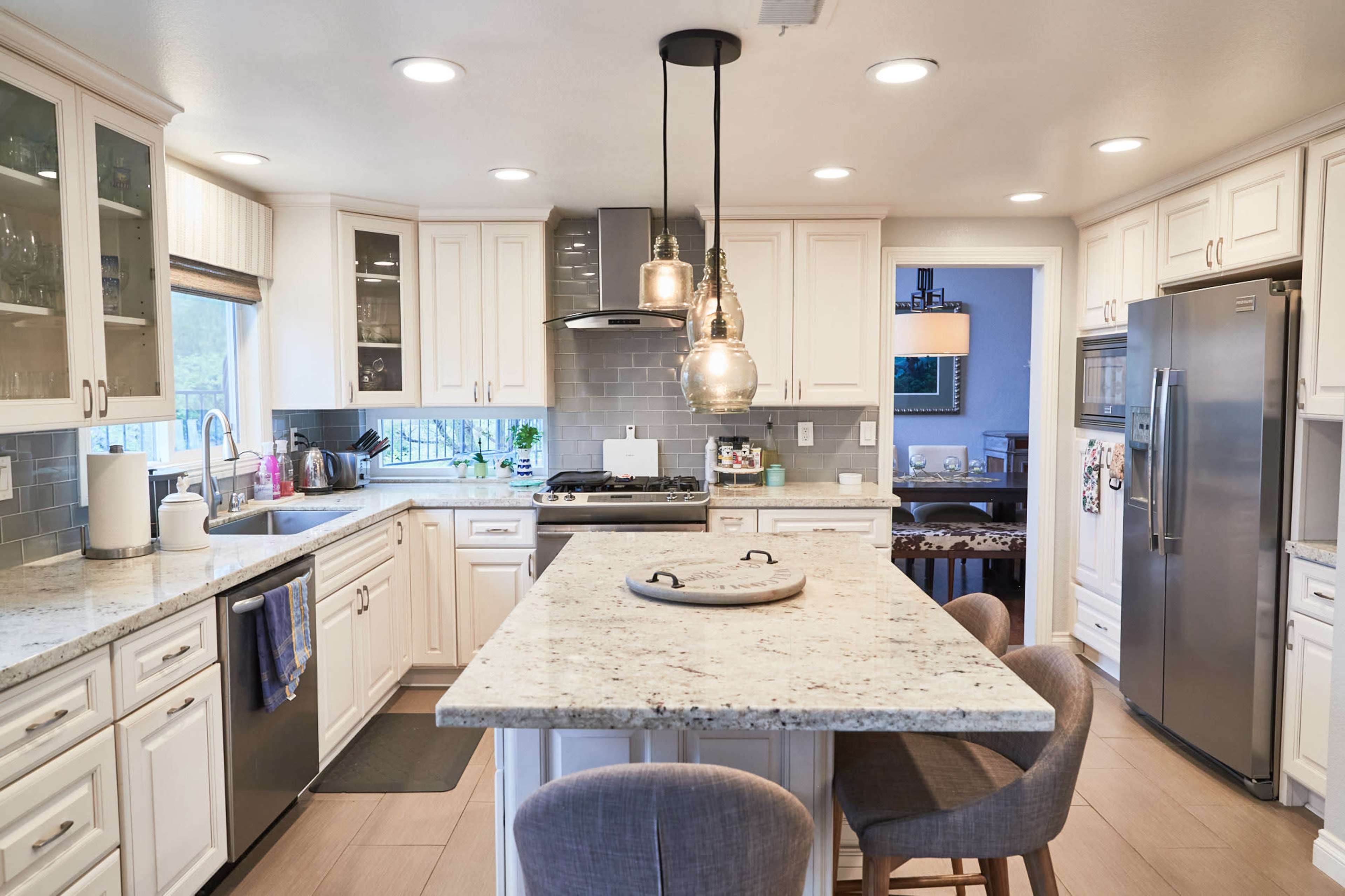 A modern kitchen features white cabinetry, granite countertops, an island with seating, and stainless steel appliances.