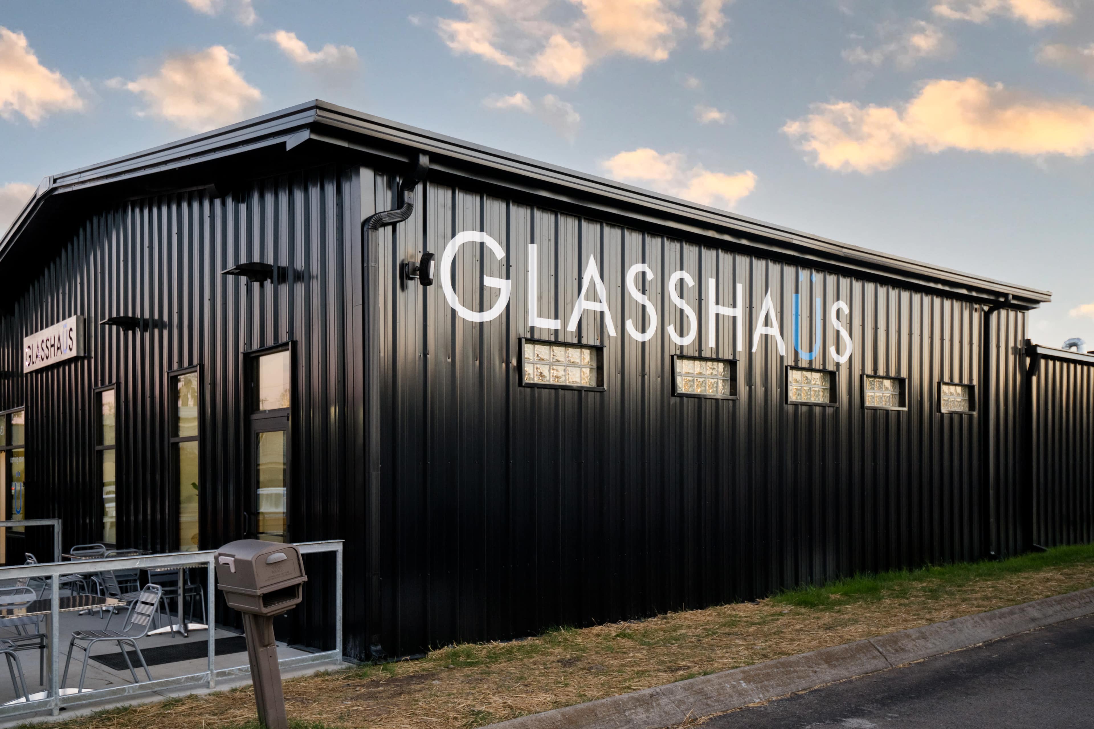 The image shows a modern black metal building with large windows and the name "GLASSHAUS" displayed prominently on one side.