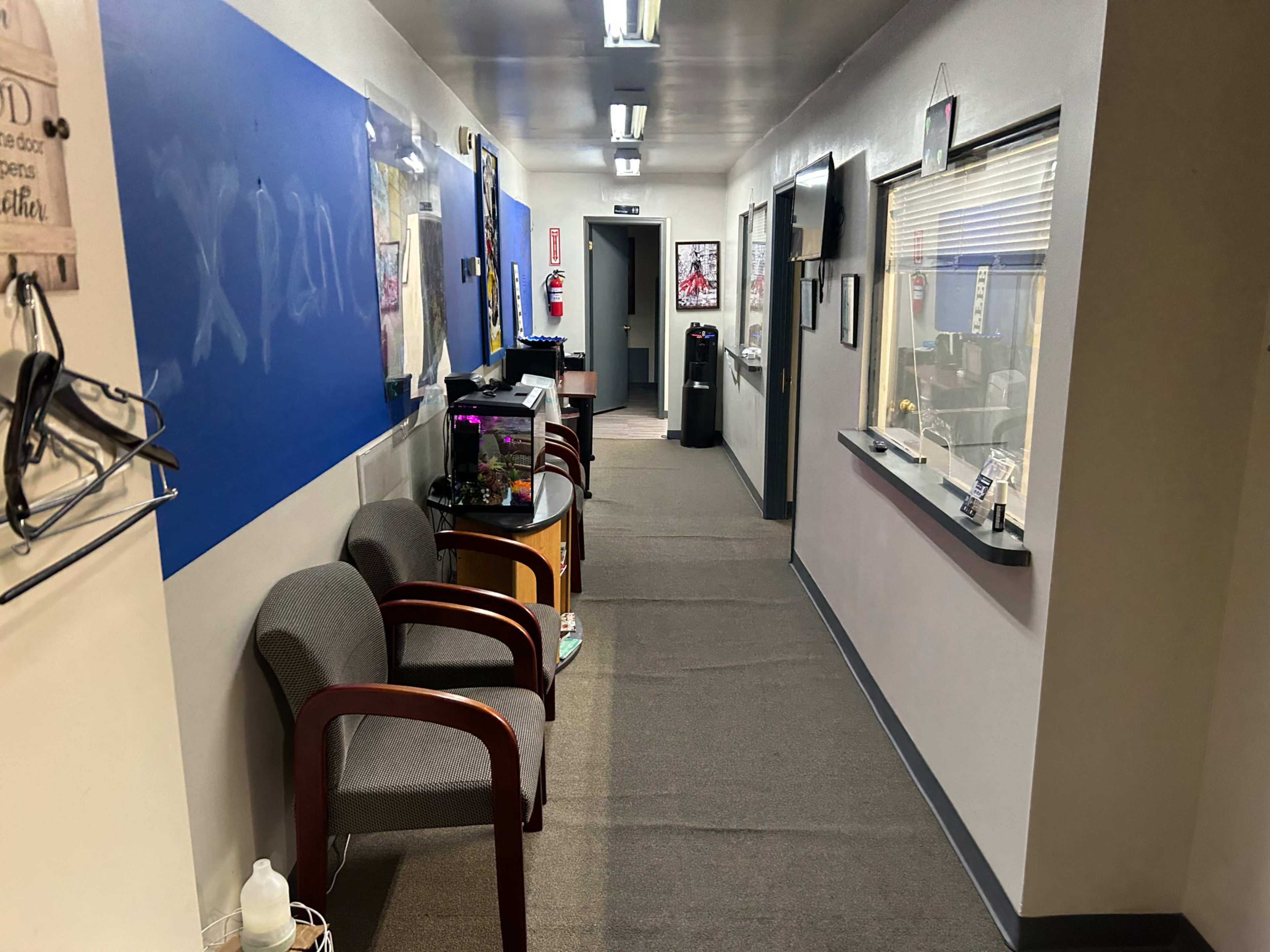 The image shows a corridor with two chairs, a fish tank on a table, and offices along the walls.