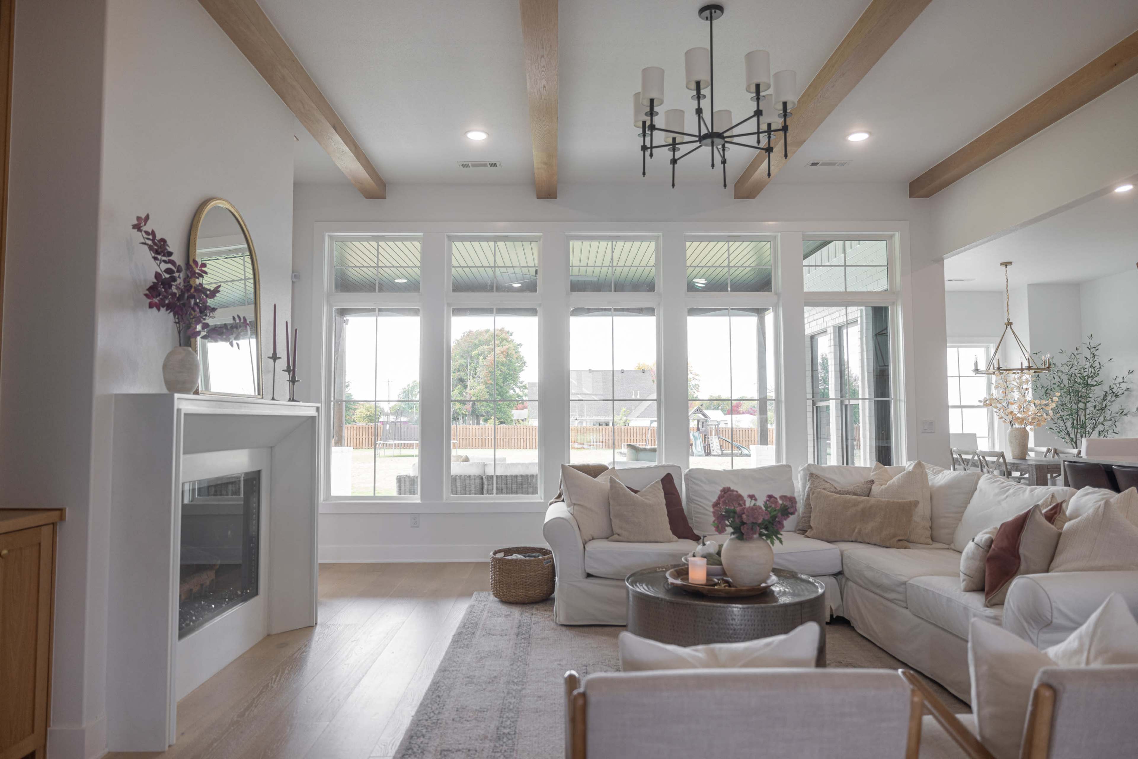 A bright living room features large windows, a white sectional sofa, and a fireplace, with wooden beams accenting the ceiling.