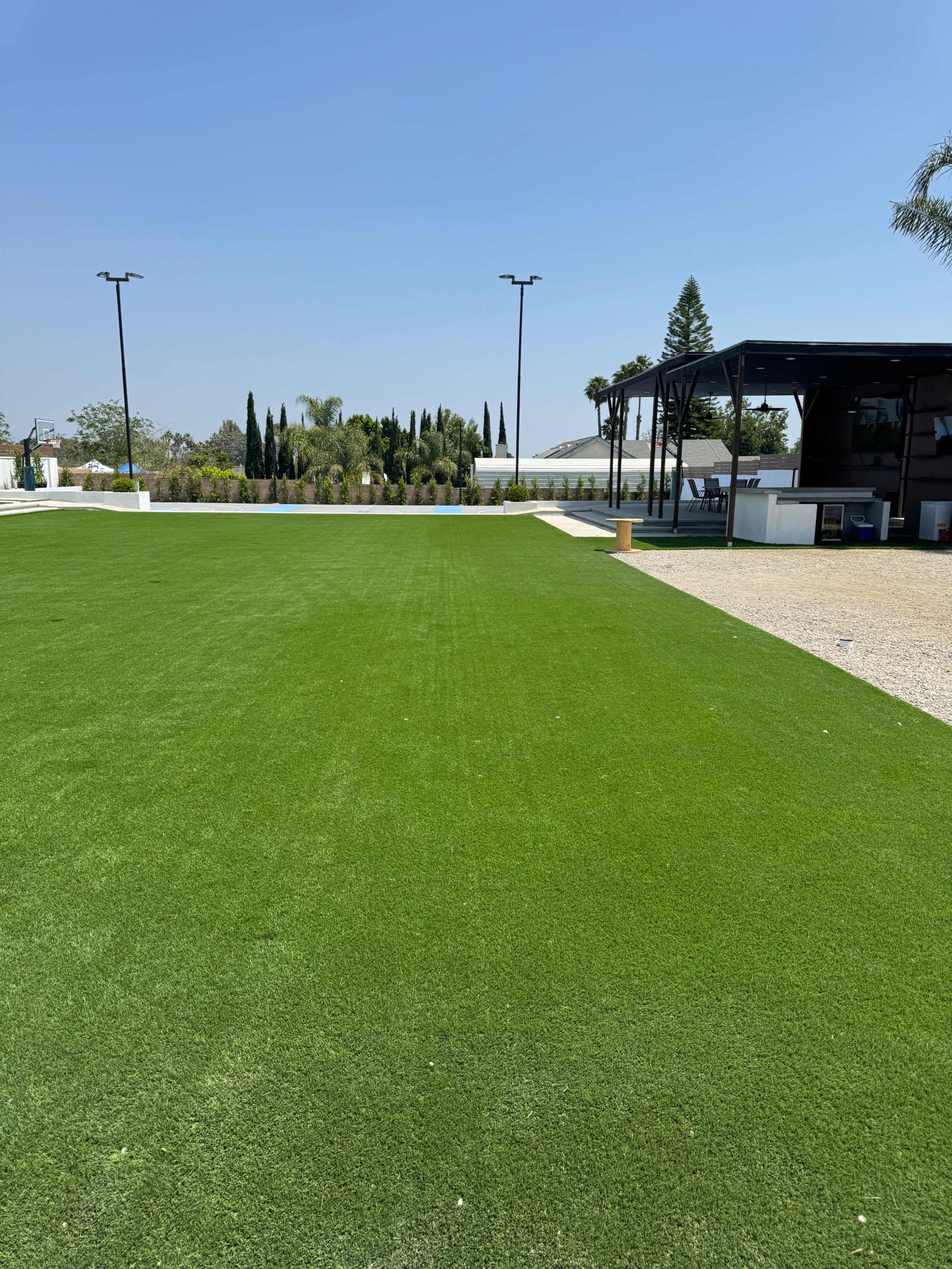 A well-manicured lawn of artificial grass is visible, bordered by palm trees and a modern outdoor structure in the background.