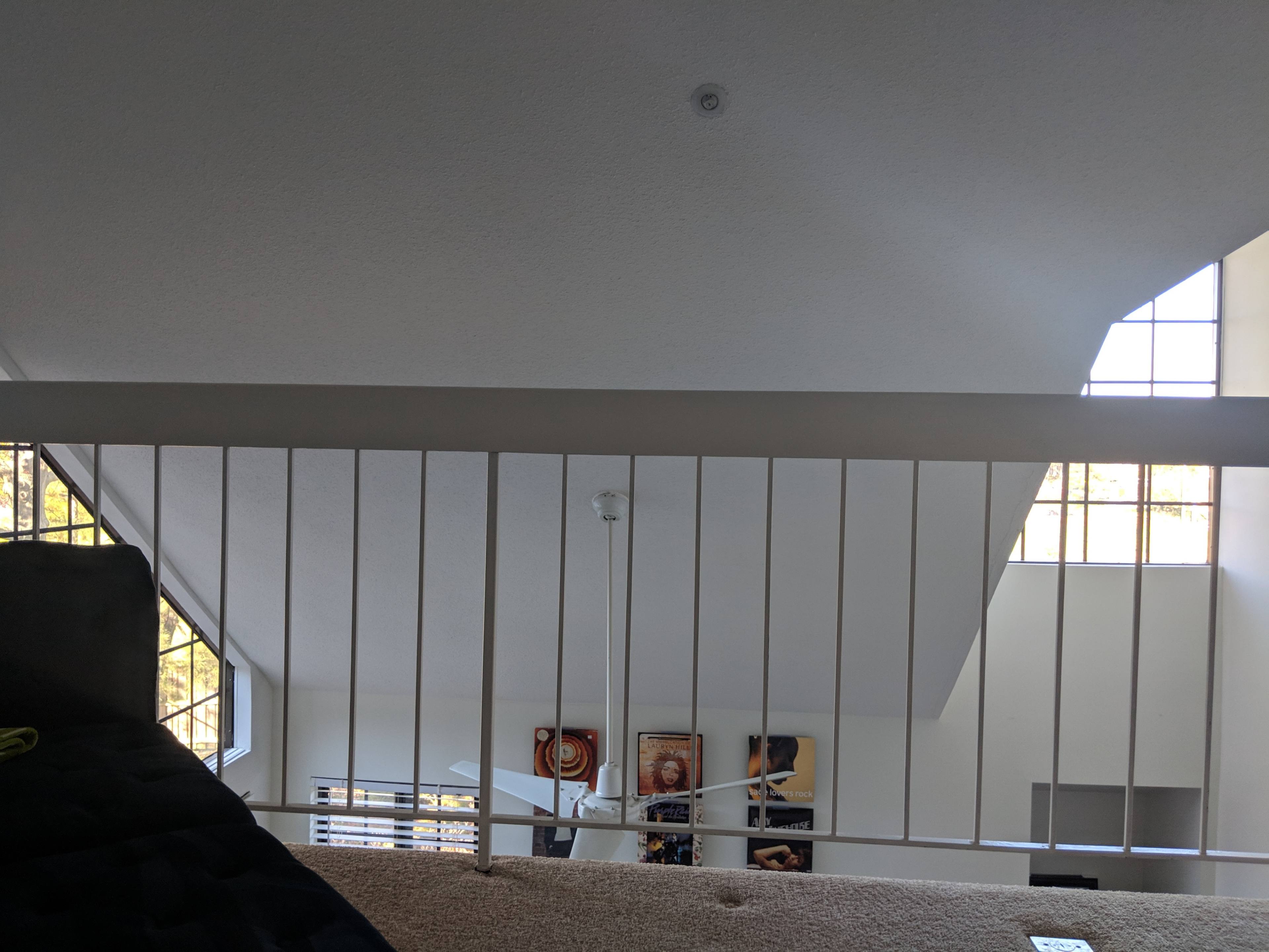 A view from an upper level looking down through a white railing into a spacious room with large windows and ceiling fans.