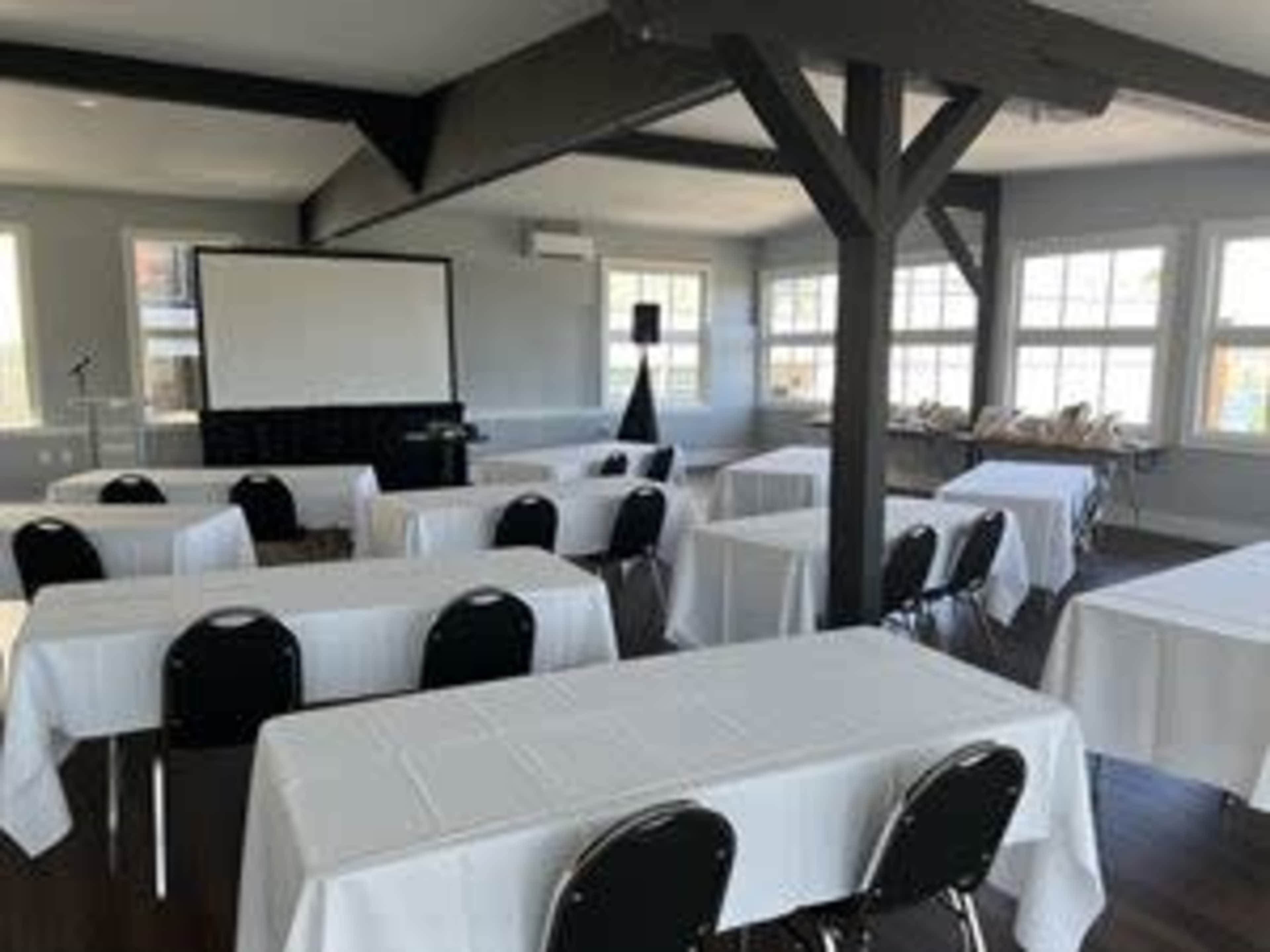 A conference room set up with several tables covered in white tablecloths and a blank screen at the front.