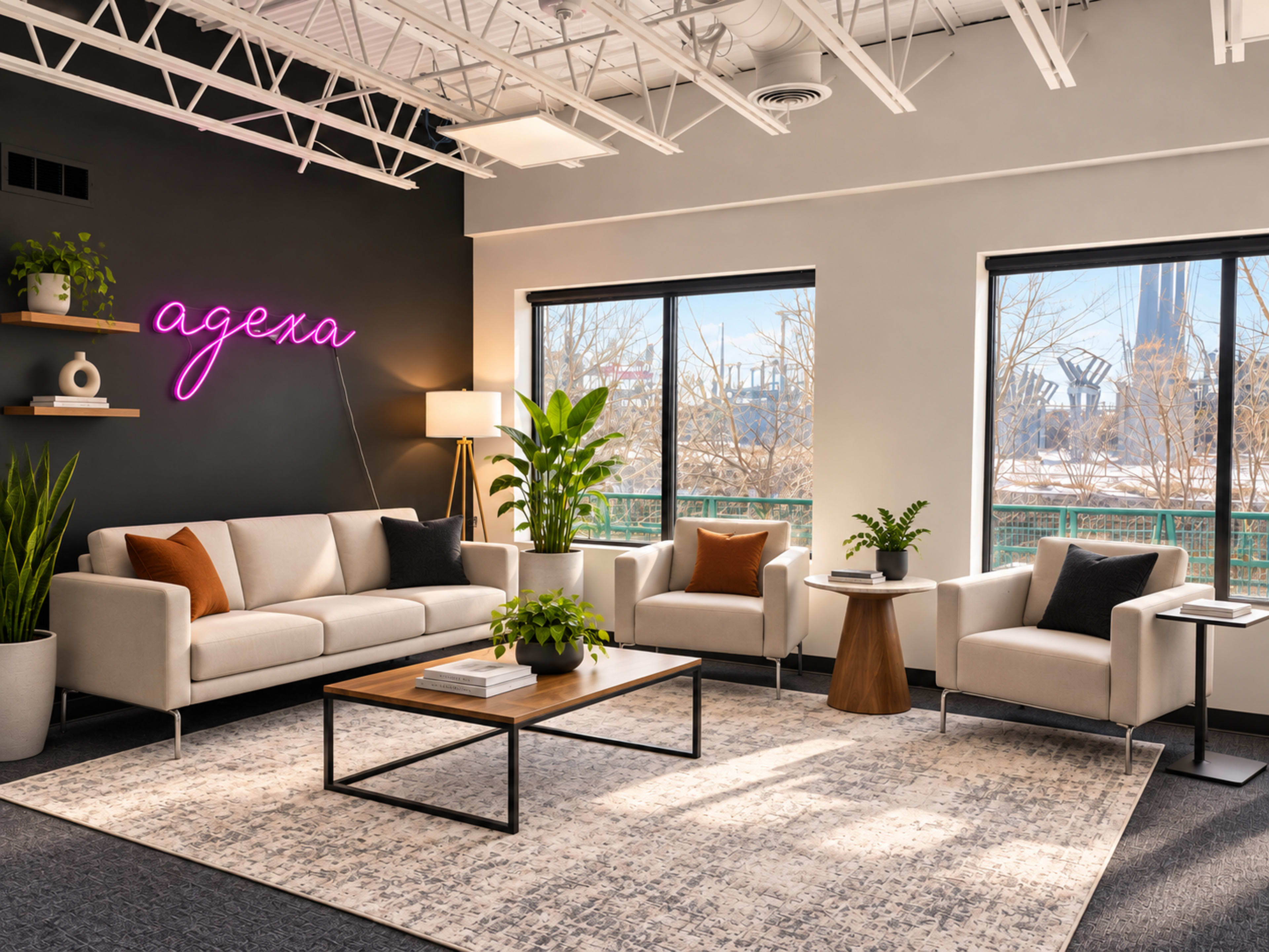 The image shows a modern office lounge with a beige couch, two armchairs, a coffee table, and large windows overlooking a cityscape, illuminated by a neon sign.