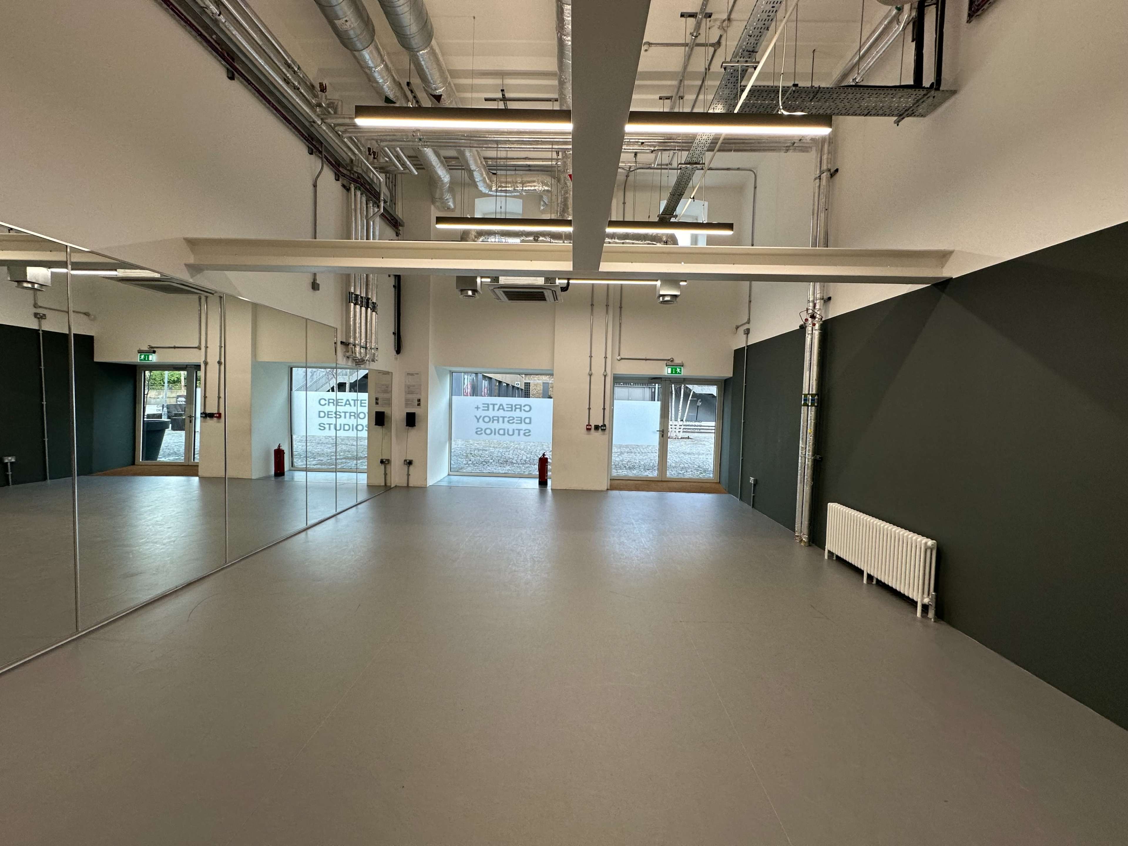 An empty studio space with large mirrors on one wall, green accent walls, and a door leading outside.