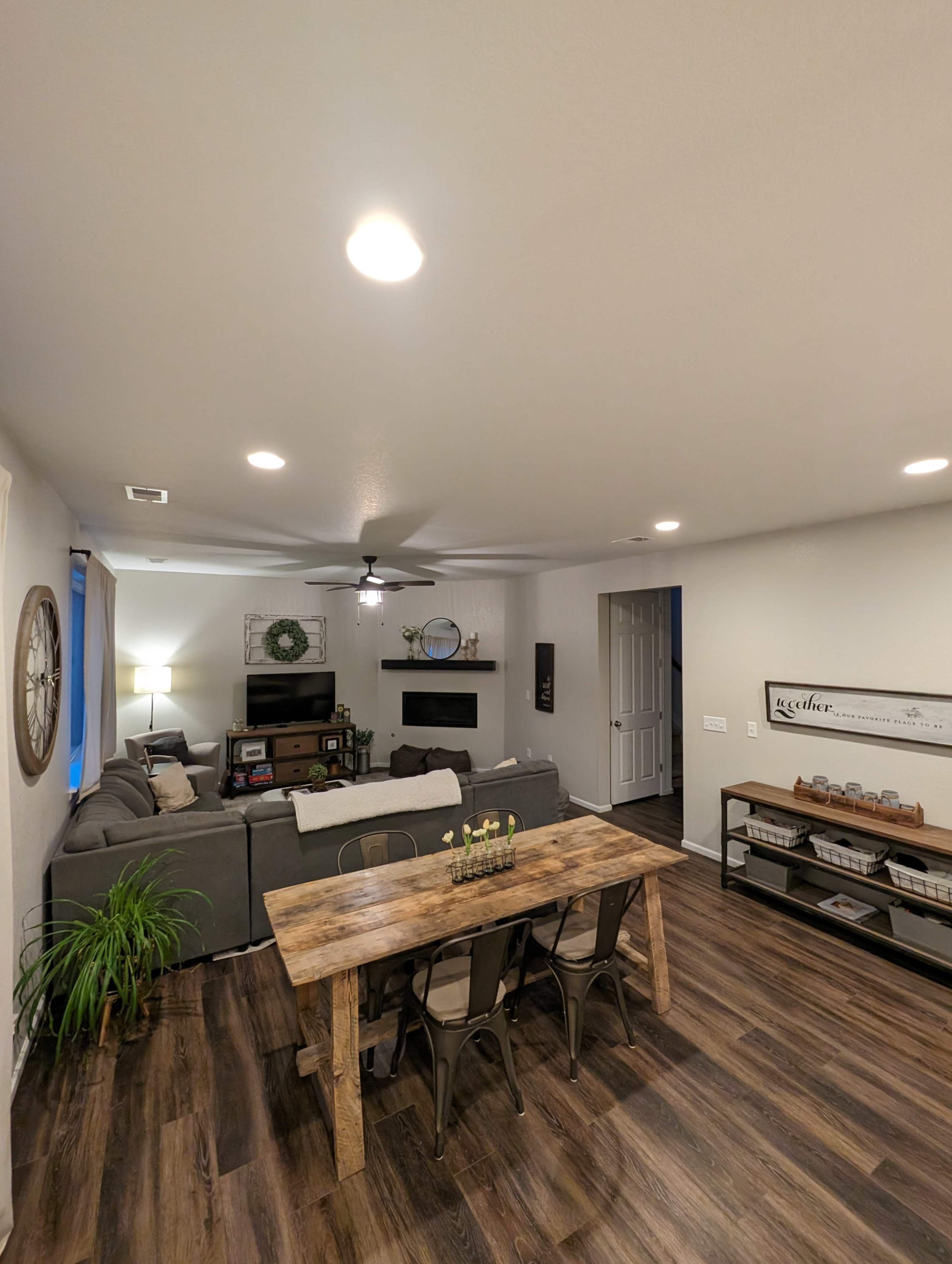 A living area featuring a gray sectional sofa, a wooden dining table with metal chairs, and a decorative shelf on the wall.