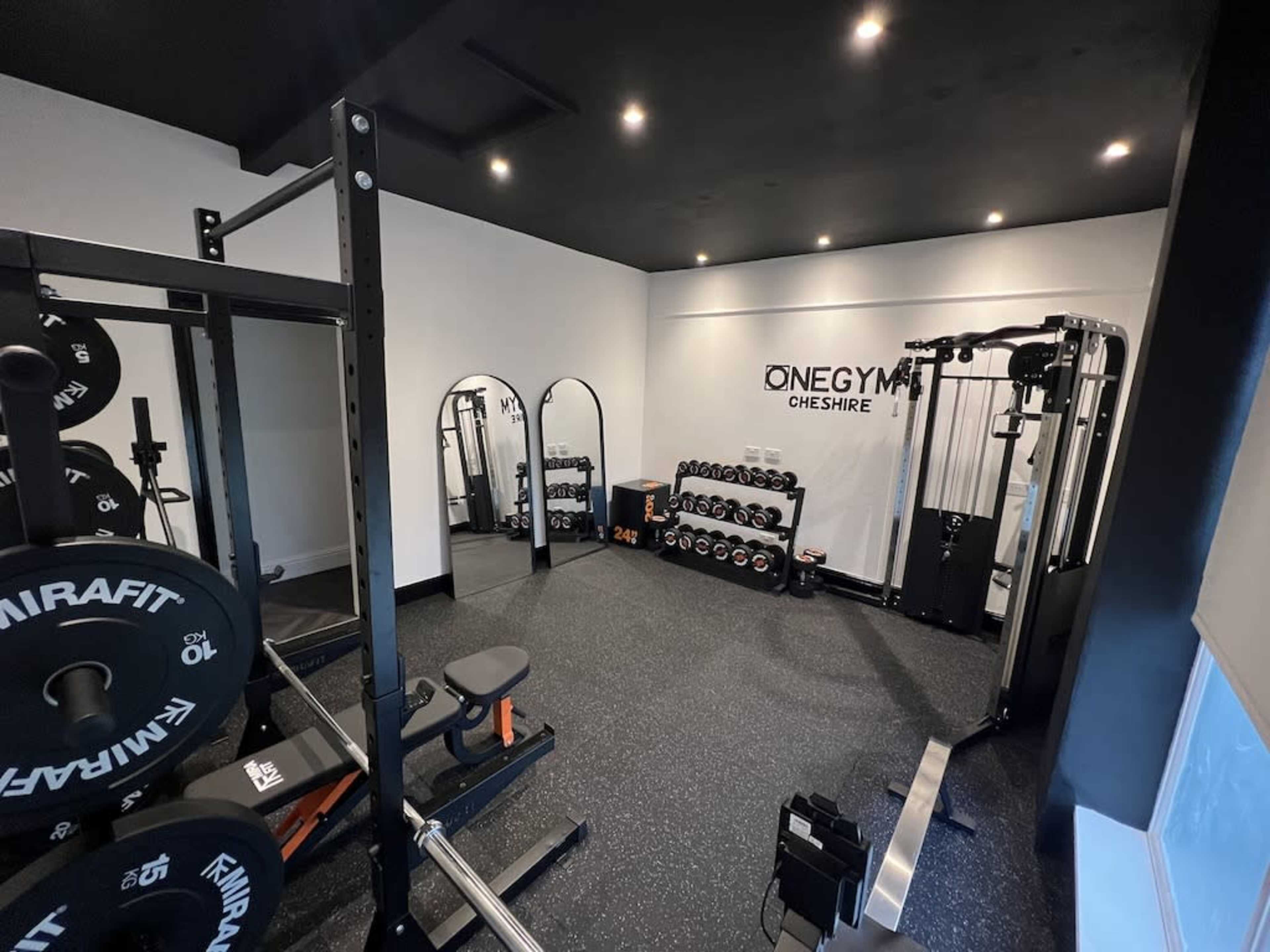 A well-equipped gym with various weightlifting equipment, mirrors, and a selection of dumbbells neatly arranged on a rack.