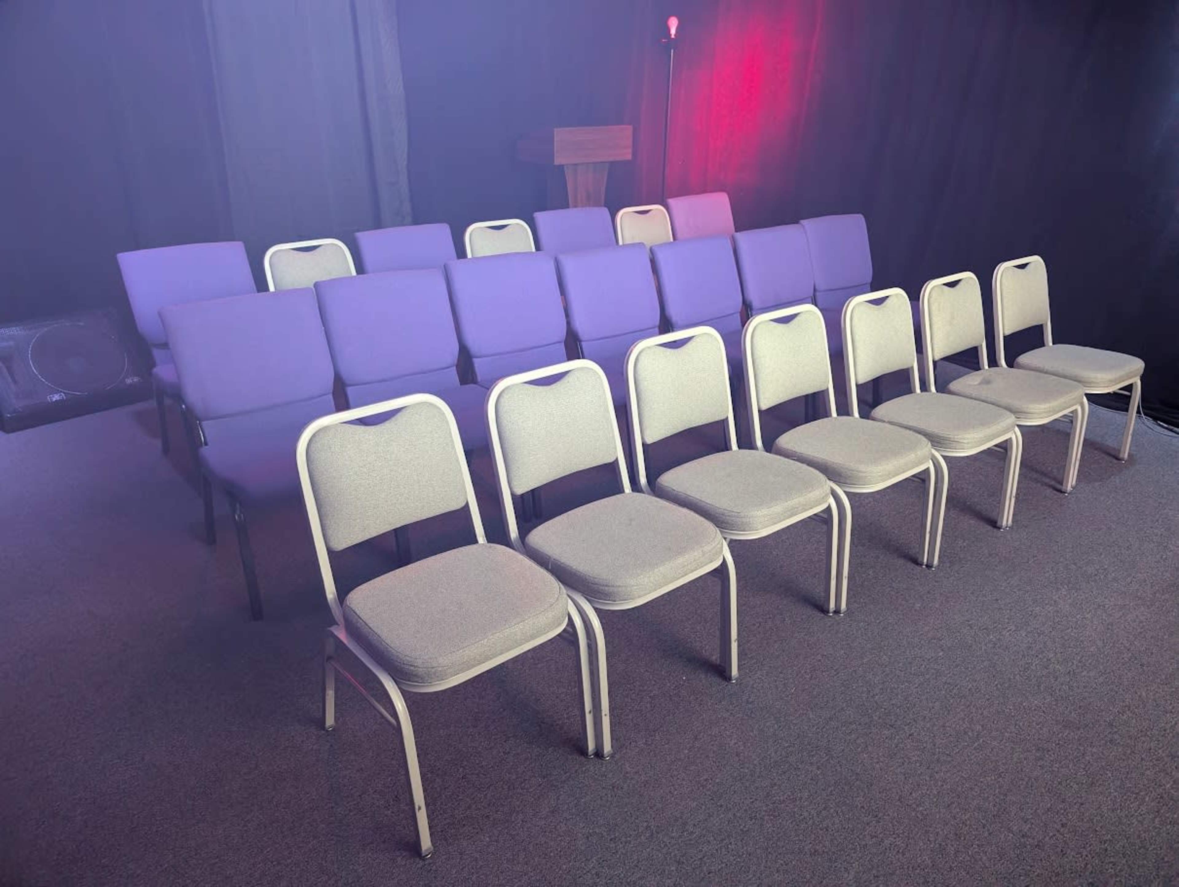 The image shows two rows of chairs, with one row of purple upholstered chairs behind a row of gray metal-framed chairs, all arranged in a dimly lit space.