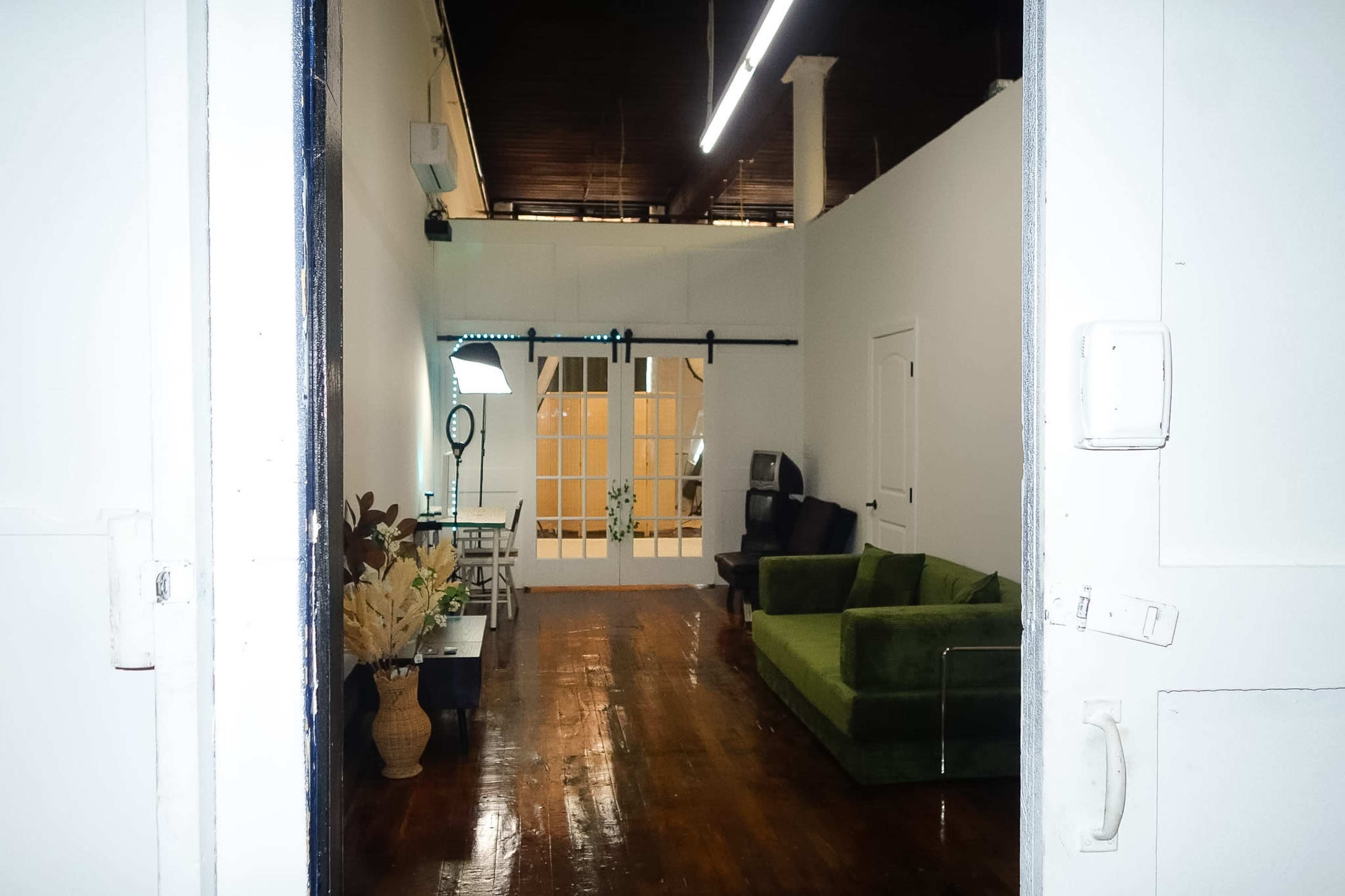 The image shows a spacious room with a green sofa, a small table, and a large window allowing natural light to enter.
