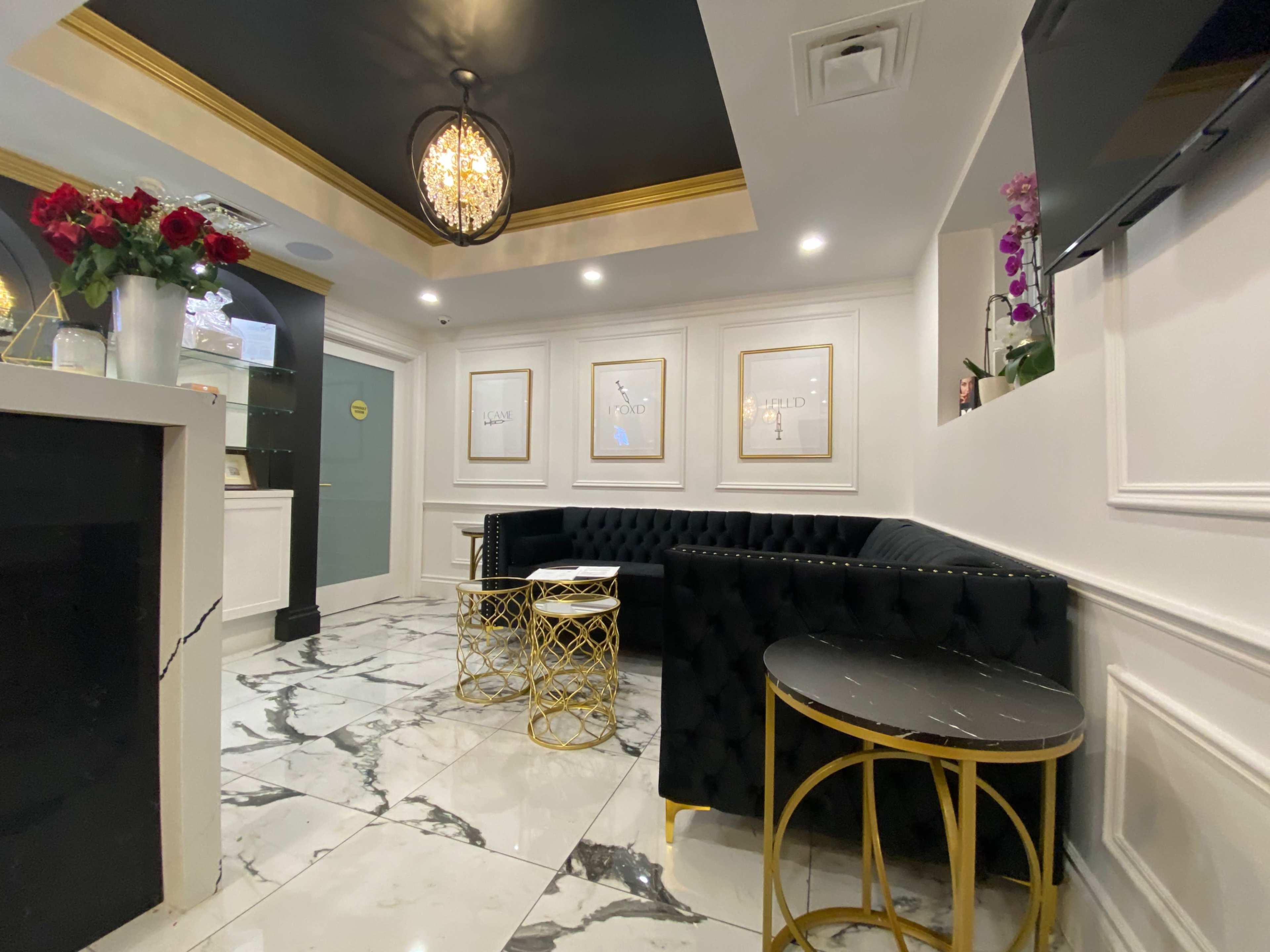 A stylish interior with black tufted seating, marble flooring, and framed wall art, complemented by decorative gold accents.