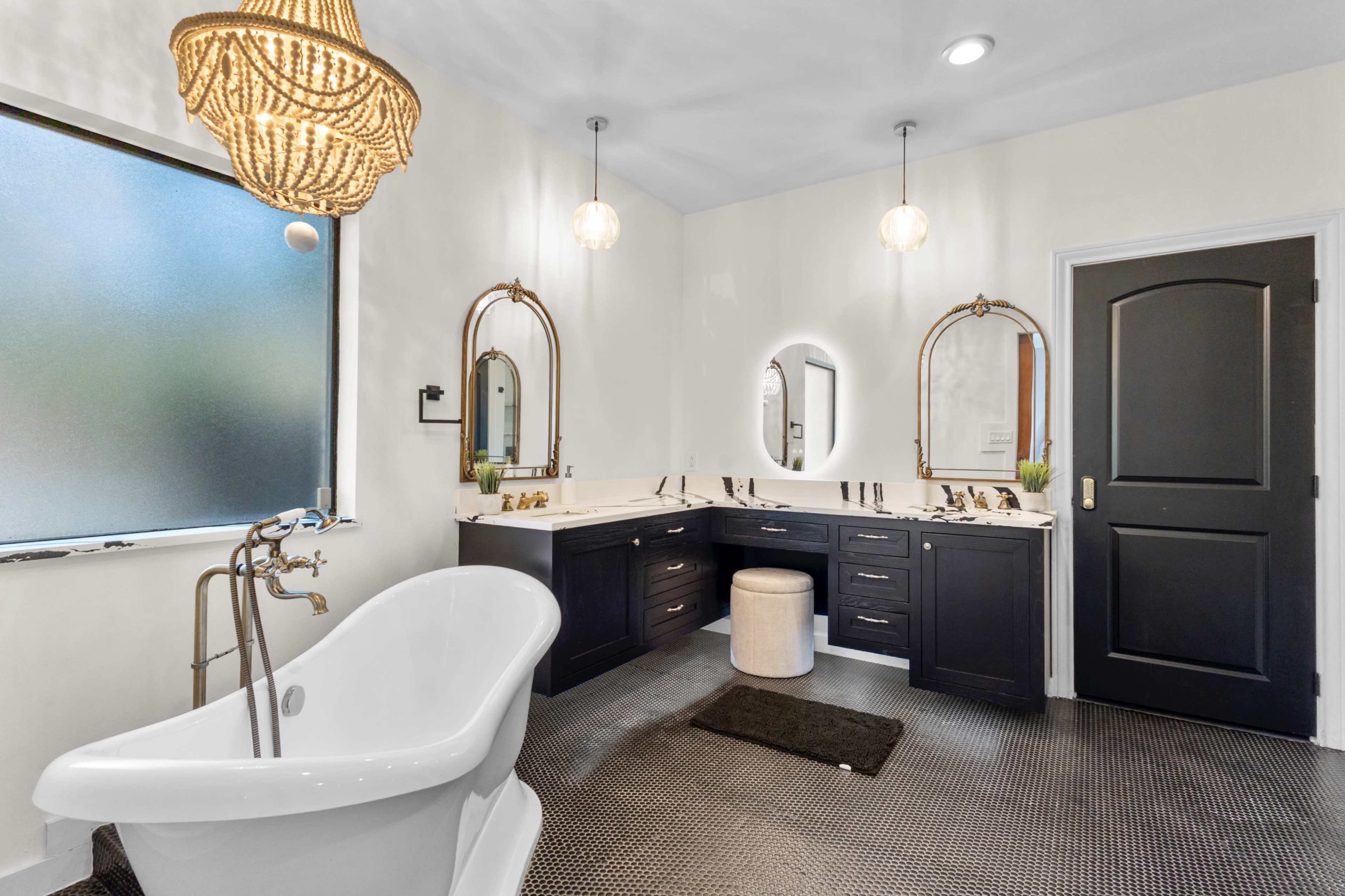 The image shows a modern bathroom featuring a freestanding bathtub, dual vanities with dark cabinetry, a chandelier, and large mirrors.