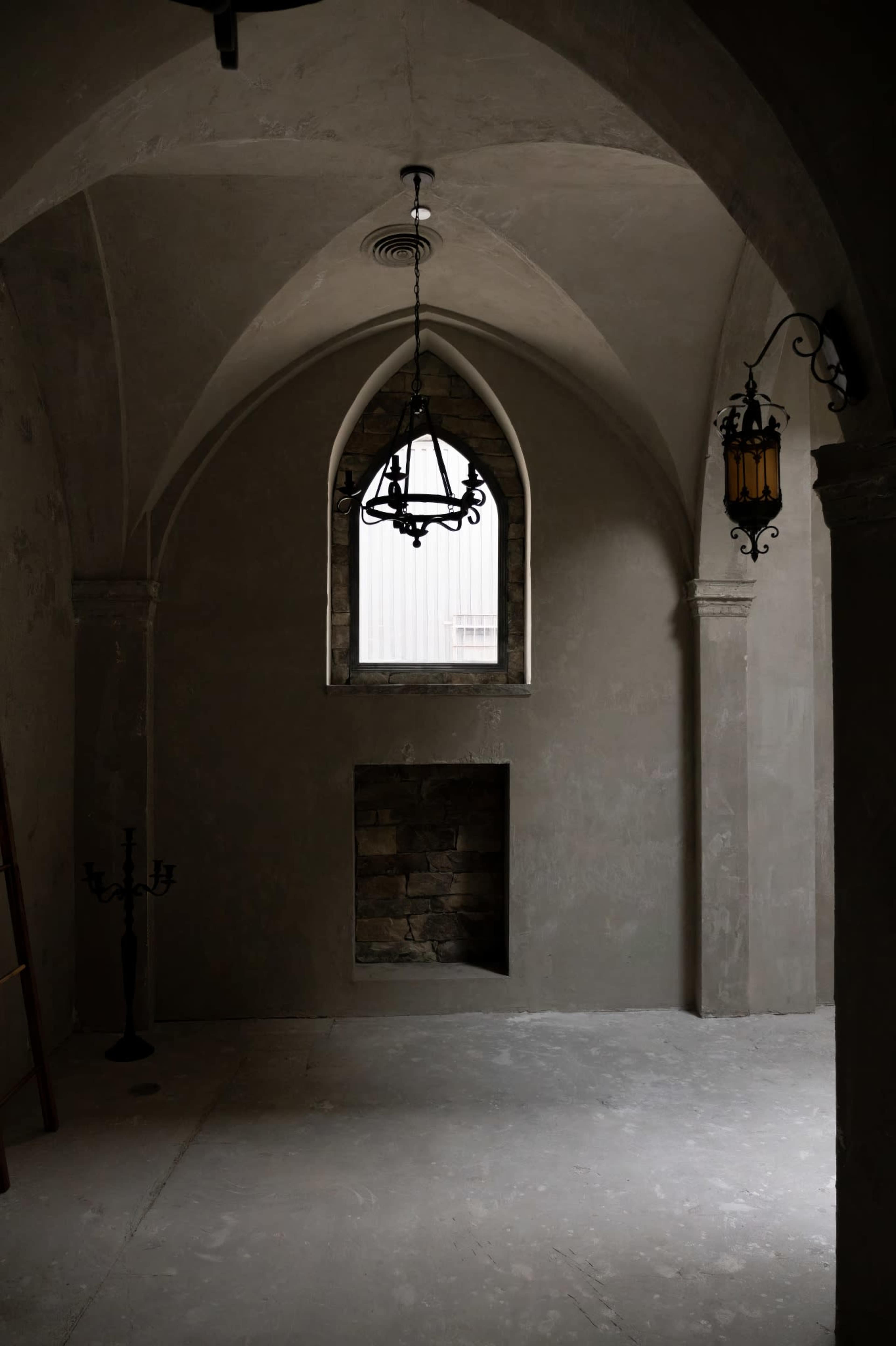 The image depicts a dimly lit stone room with arched ceilings, featuring a window, a wall-mounted lantern, and a stone recess.