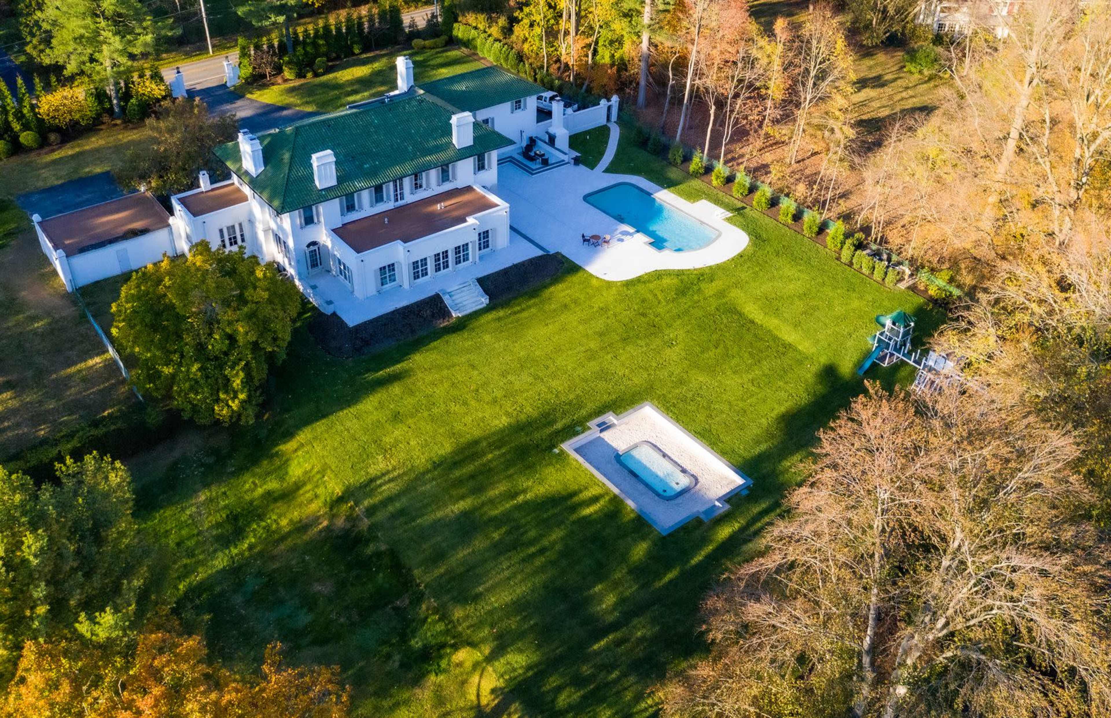 The image shows a large, modern house with a swimming pool and landscaped yard, surrounded by trees and a manicured lawn.