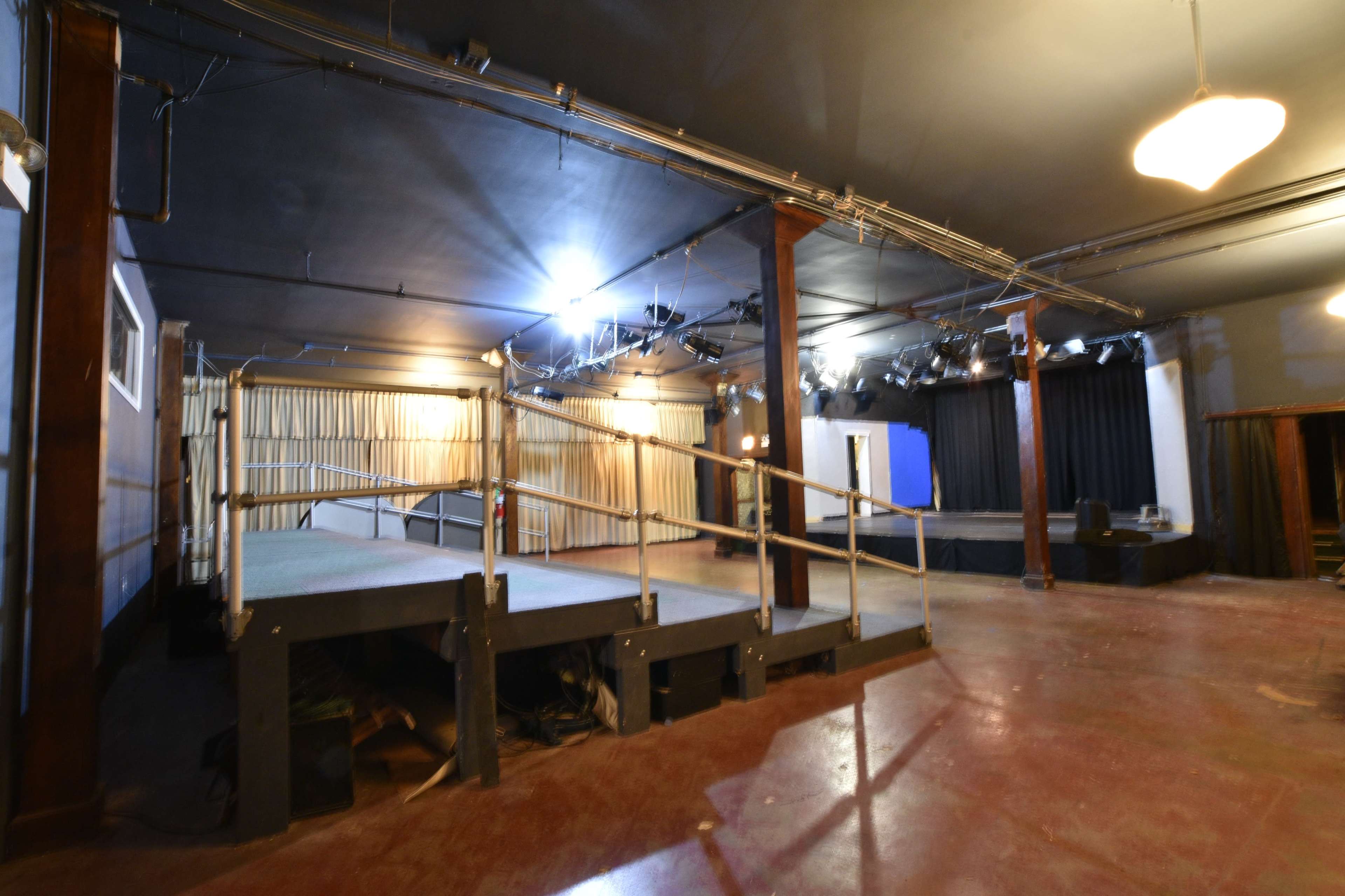 An empty performance space with staging areas, lighting rigging, and curtains along the walls.