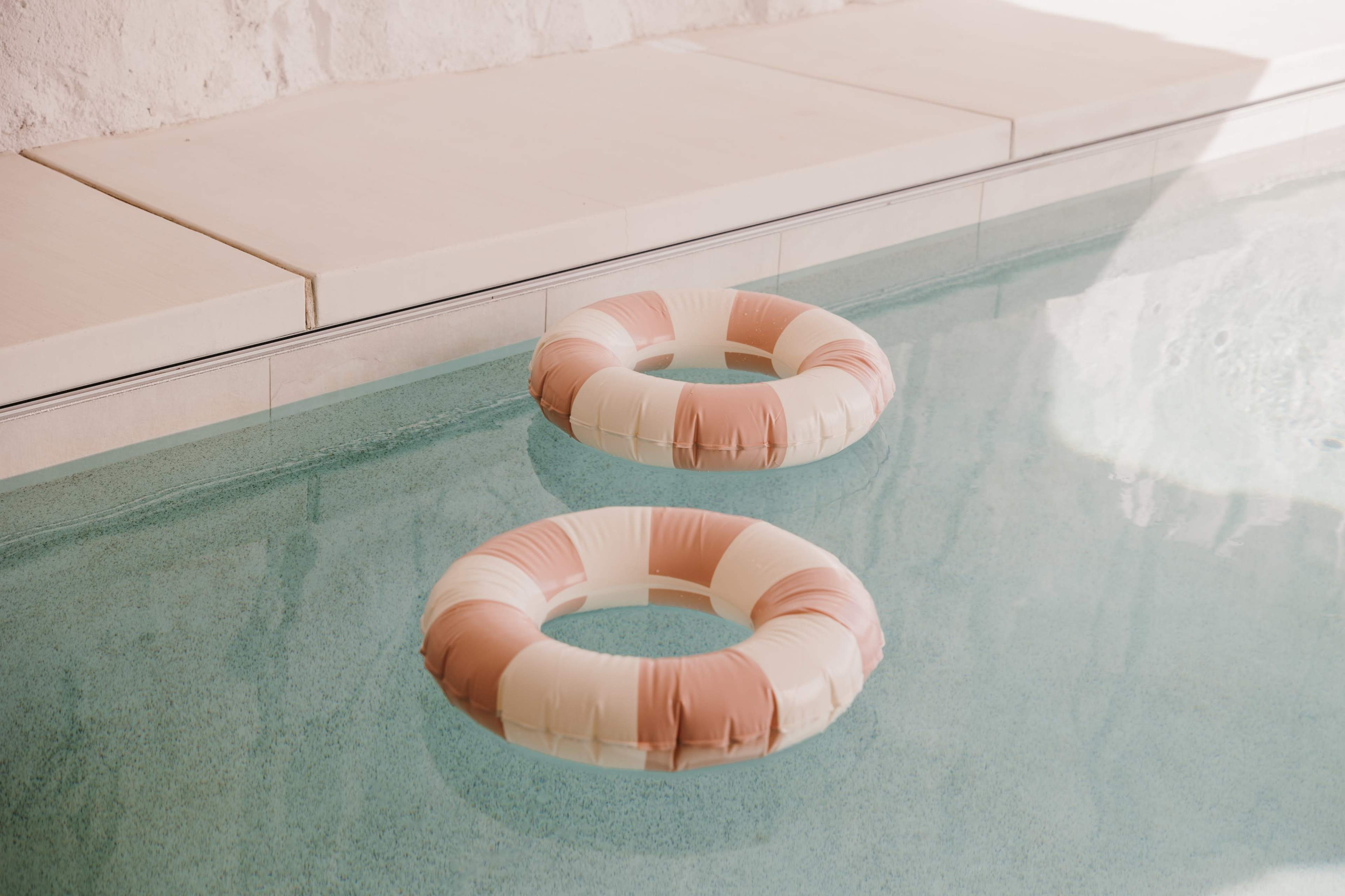 Two circular pool floats with pink and white stripes are floating on the surface of a clear swimming pool.