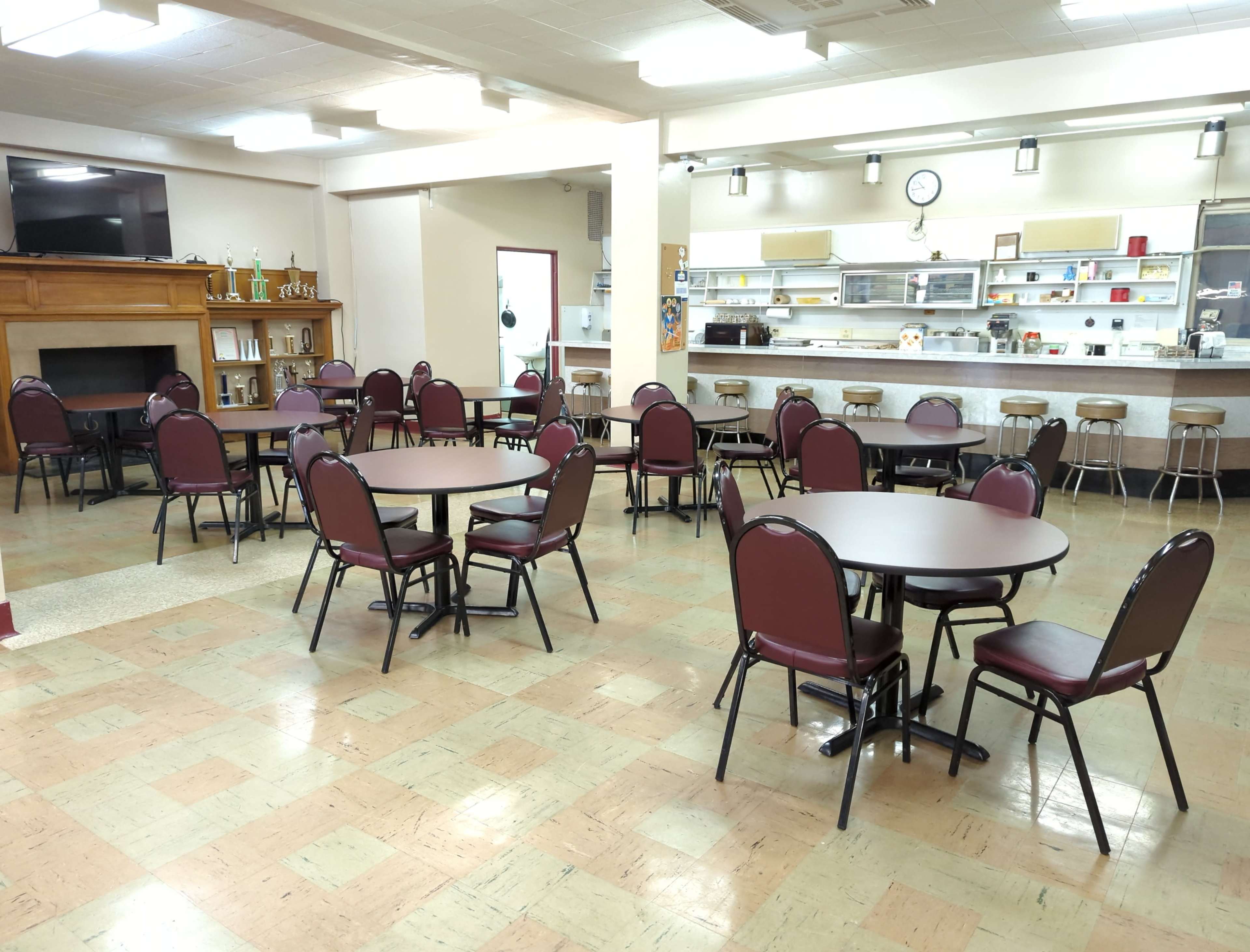 A dining area with several round tables and chairs arranged in a room featuring a counter and kitchen space in the background.