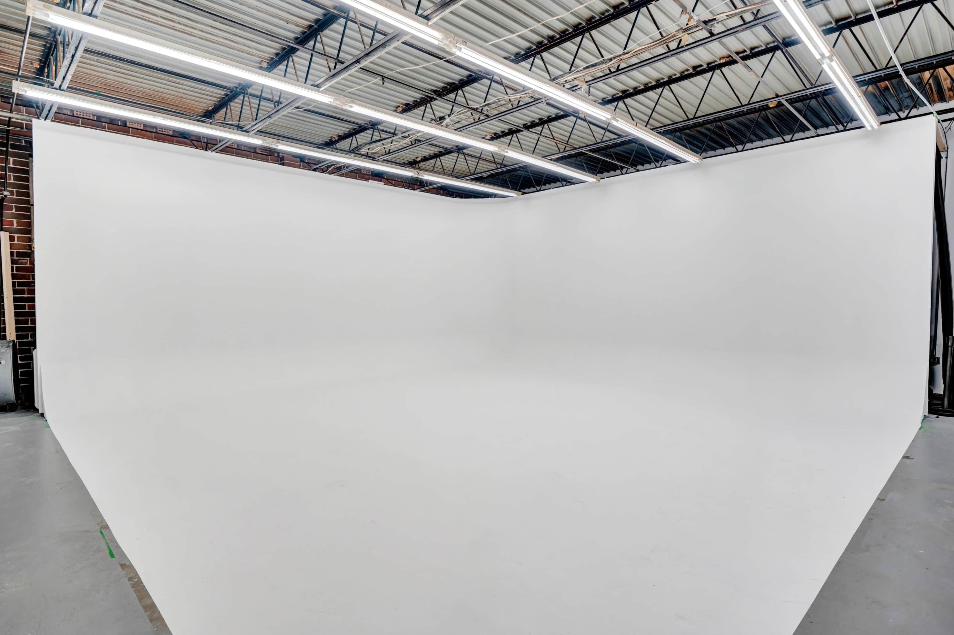 An empty studio space with a seamless white background and overhead lighting.