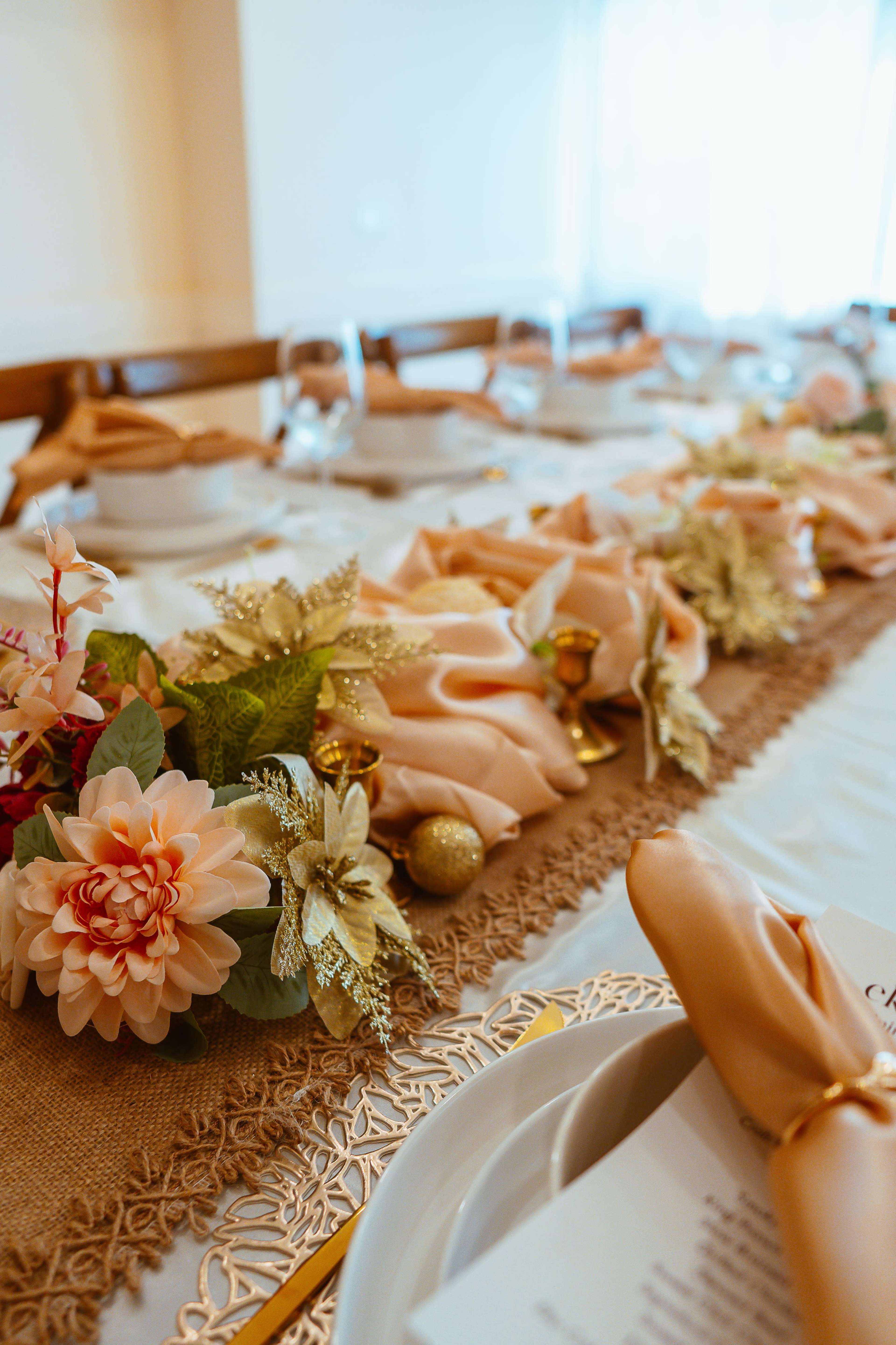 A table is set with beige linens, decorative flowers, and elegant tableware for a gathering.