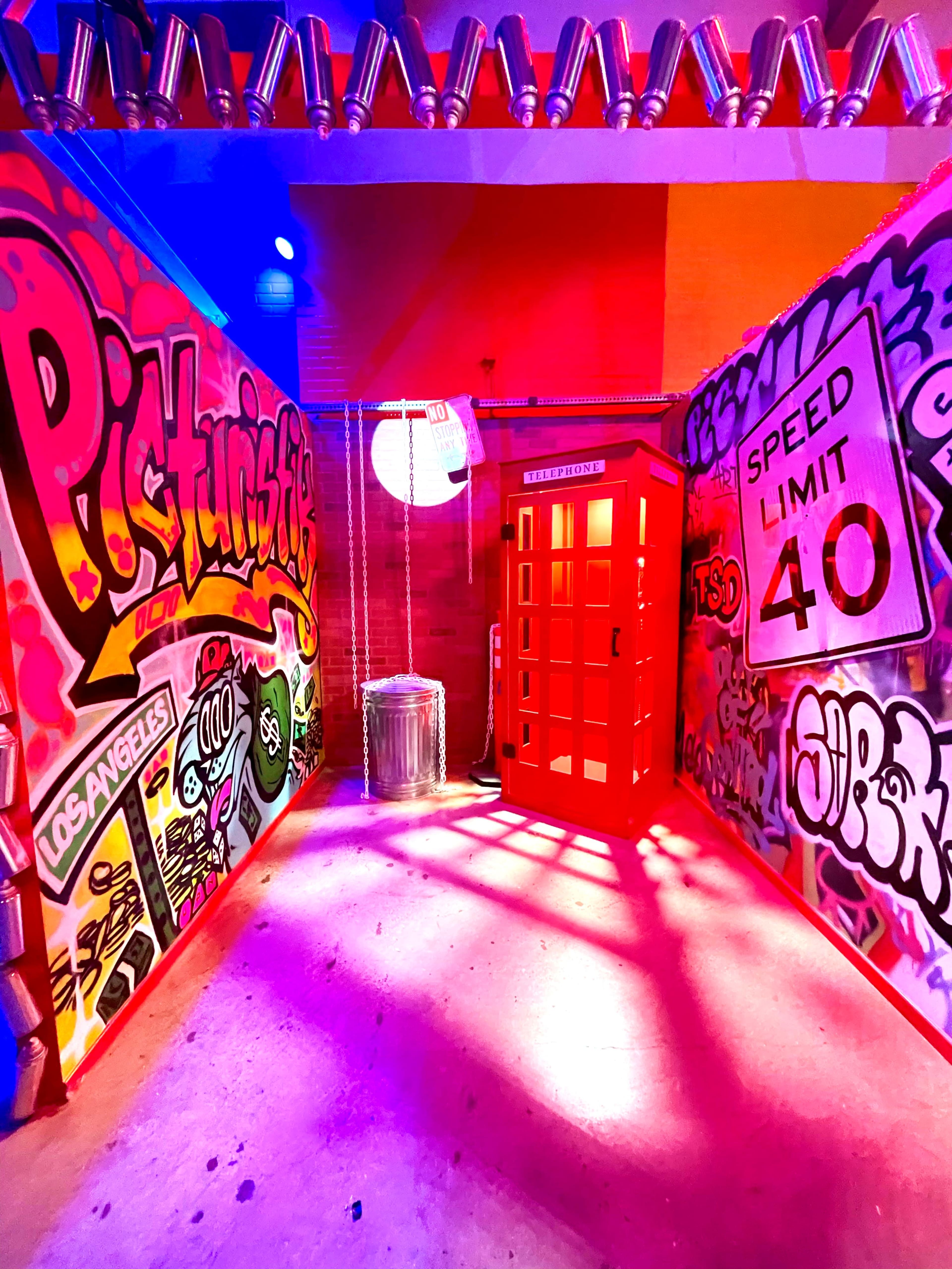 A brightly lit alleyway adorned with colorful graffiti on the walls, featuring a red telephone booth in the center.