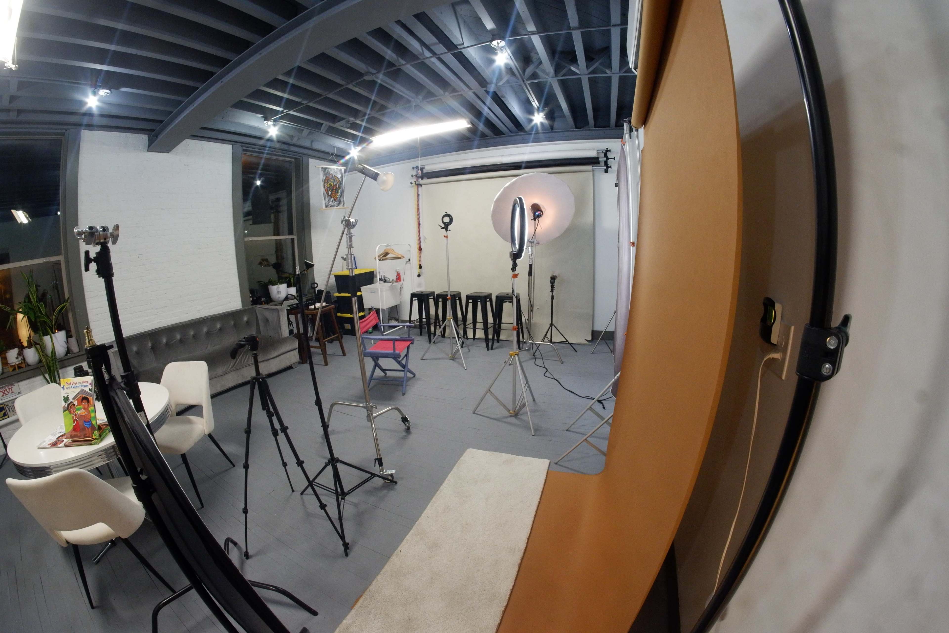 The image shows a photography studio equipped with various lighting setups, backdrops, and props arranged for a photoshoot.