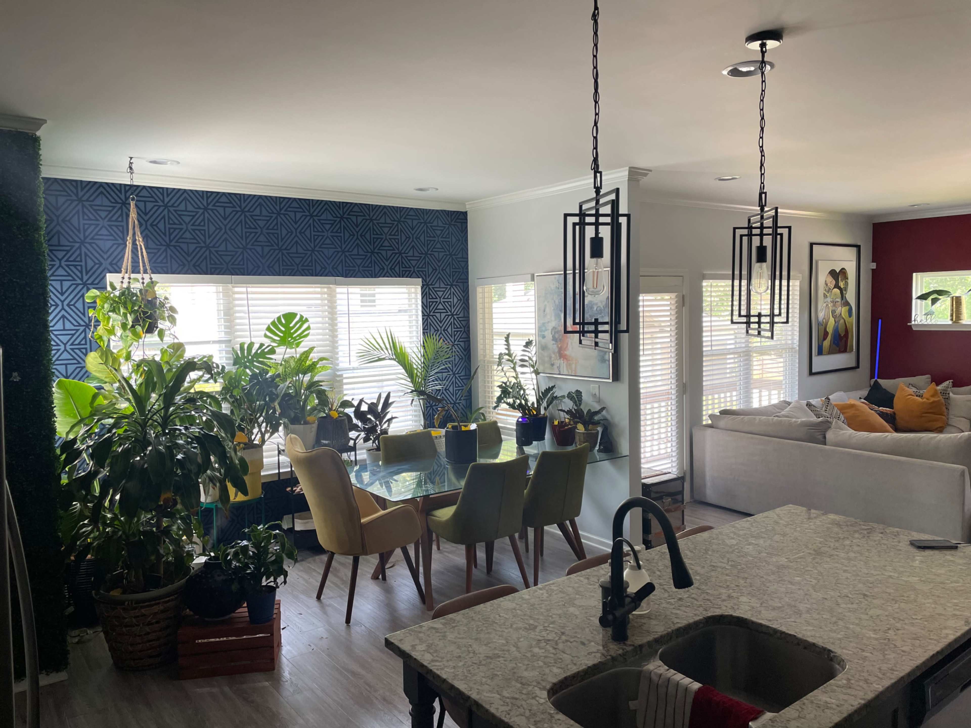 A spacious living area features a dining table surrounded by colorful chairs and various indoor plants, with a sectional sofa in the adjacent space.
