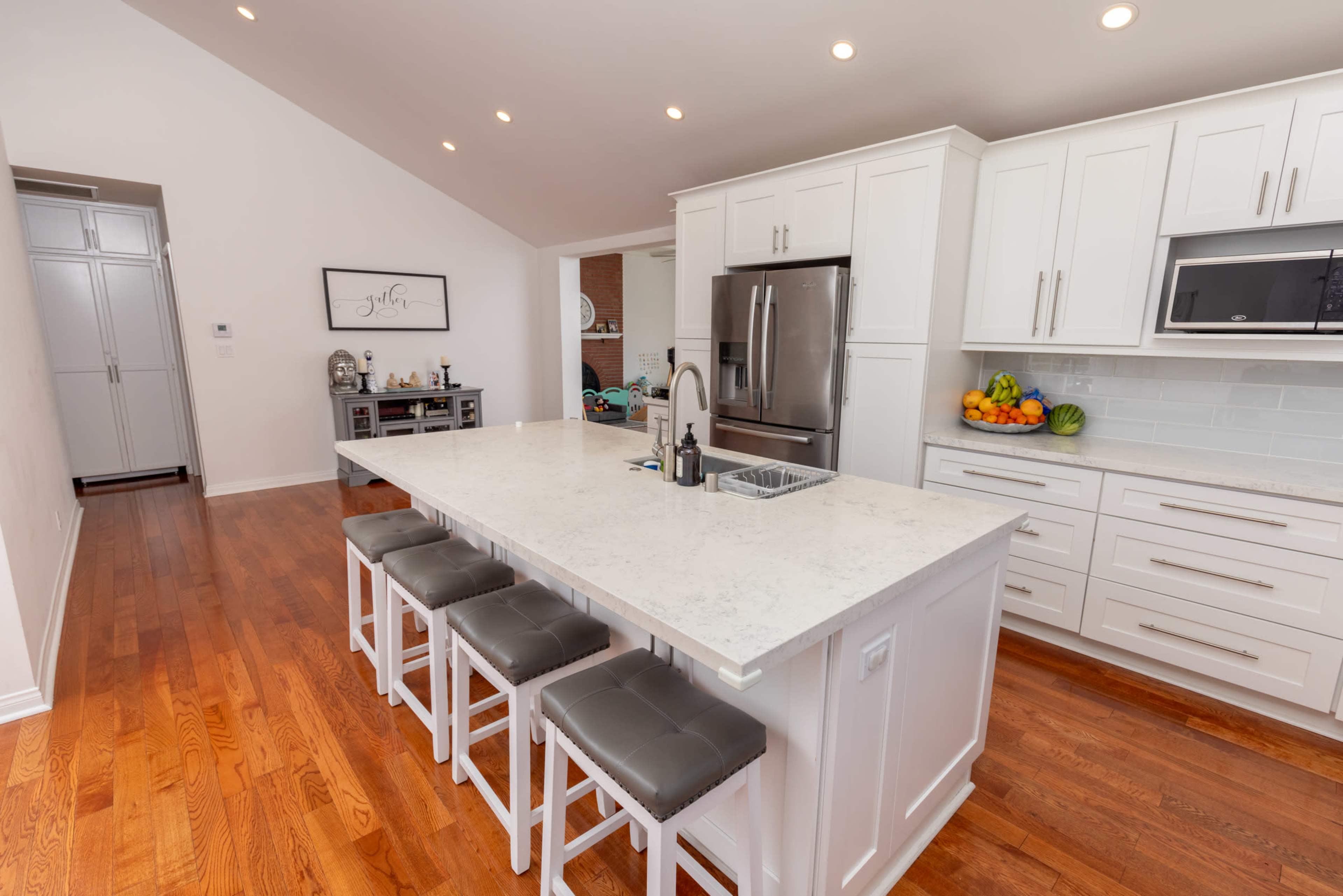 The image shows a modern kitchen with white cabinetry, a large island with bar stools, and stainless steel appliances.