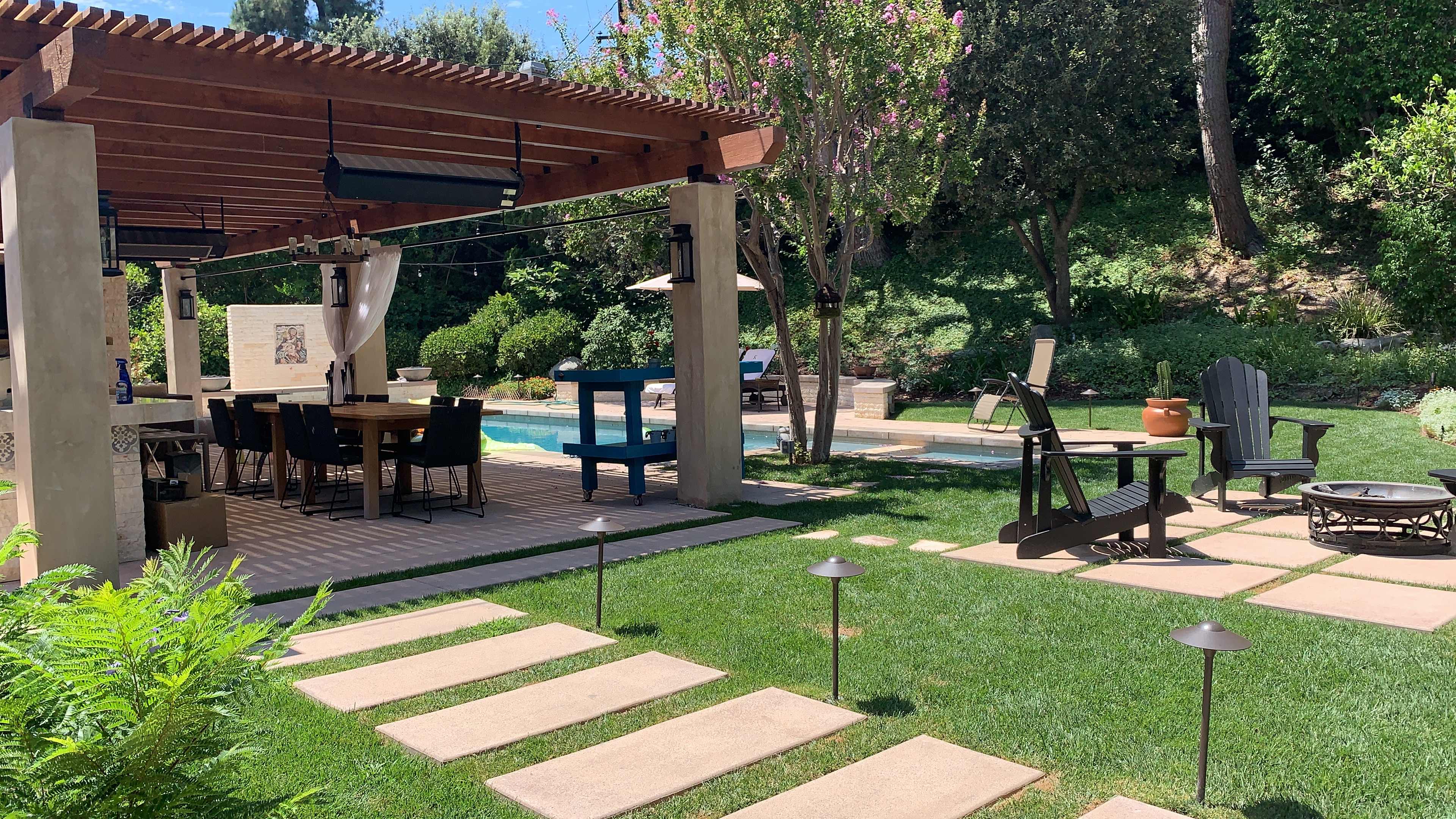 A landscaped backyard with a pool, outdoor dining area, and various seating arrangements surrounded by greenery.