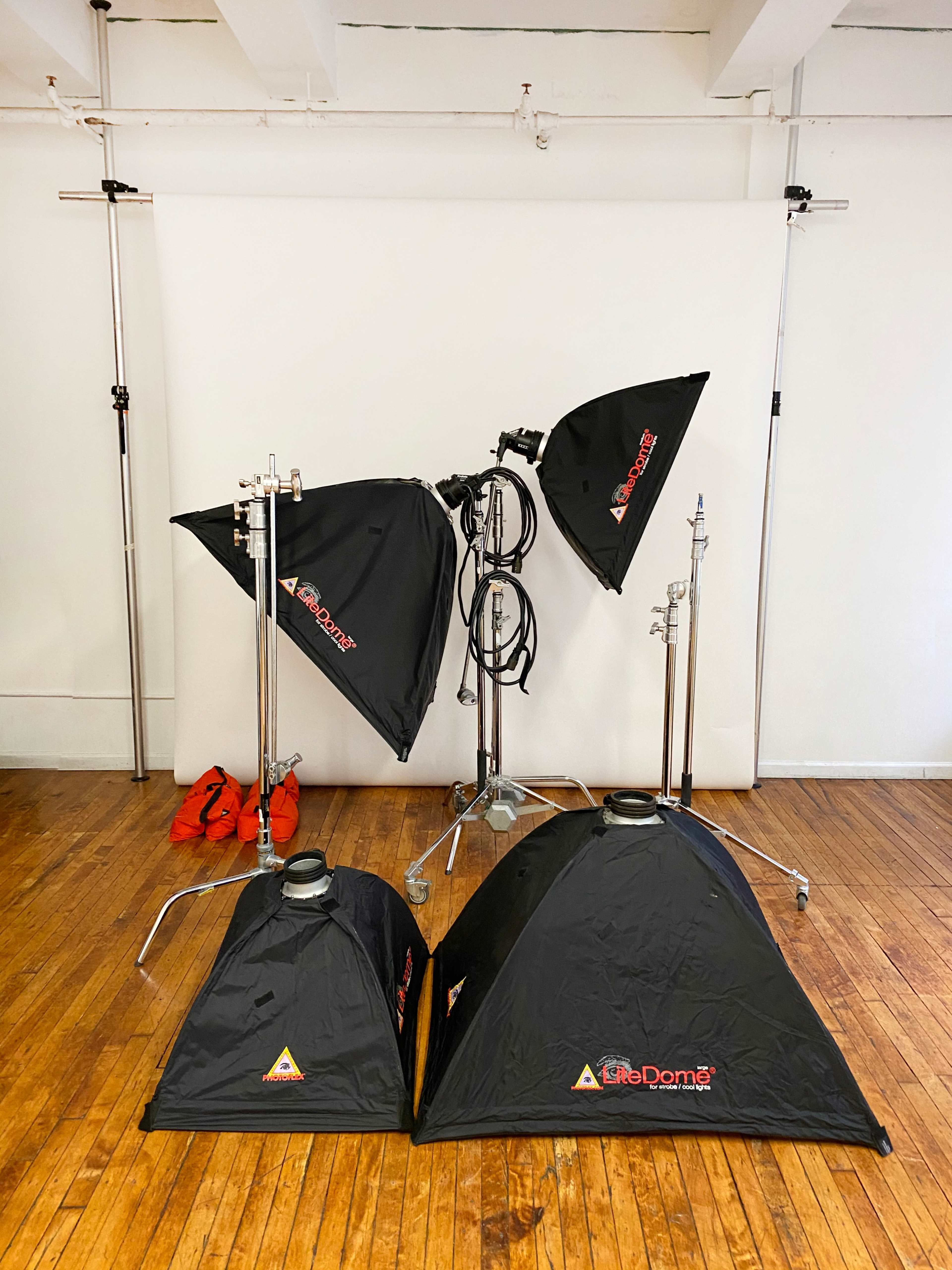 The image shows a photography studio setup with three softbox lights and two light stands on a wooden floor, against a white backdrop.