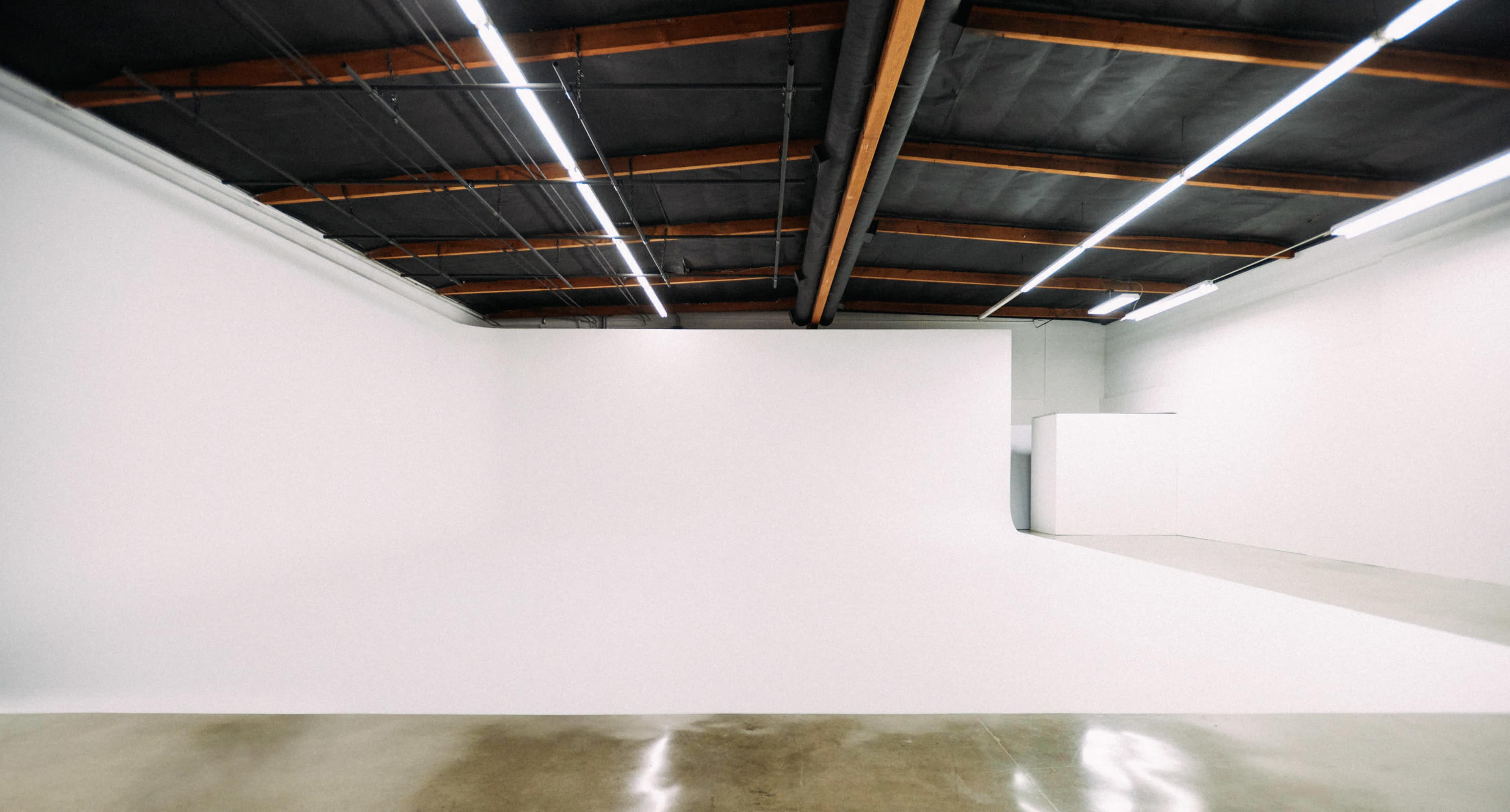 A large, empty studio space with white walls and a polished concrete floor.