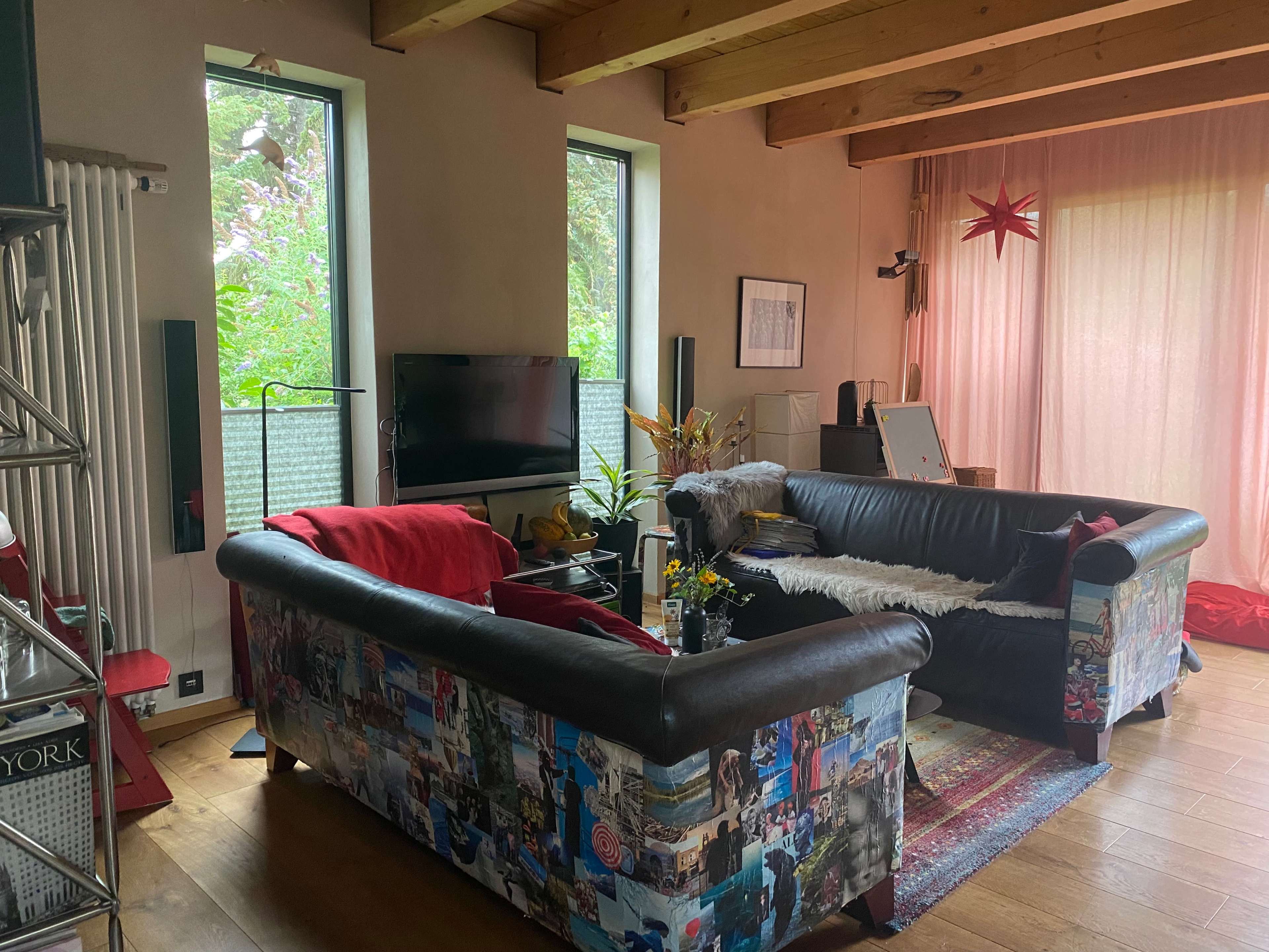 A living room with two black sofas covered in collage, a television mounted on the wall, and large windows letting in natural light.