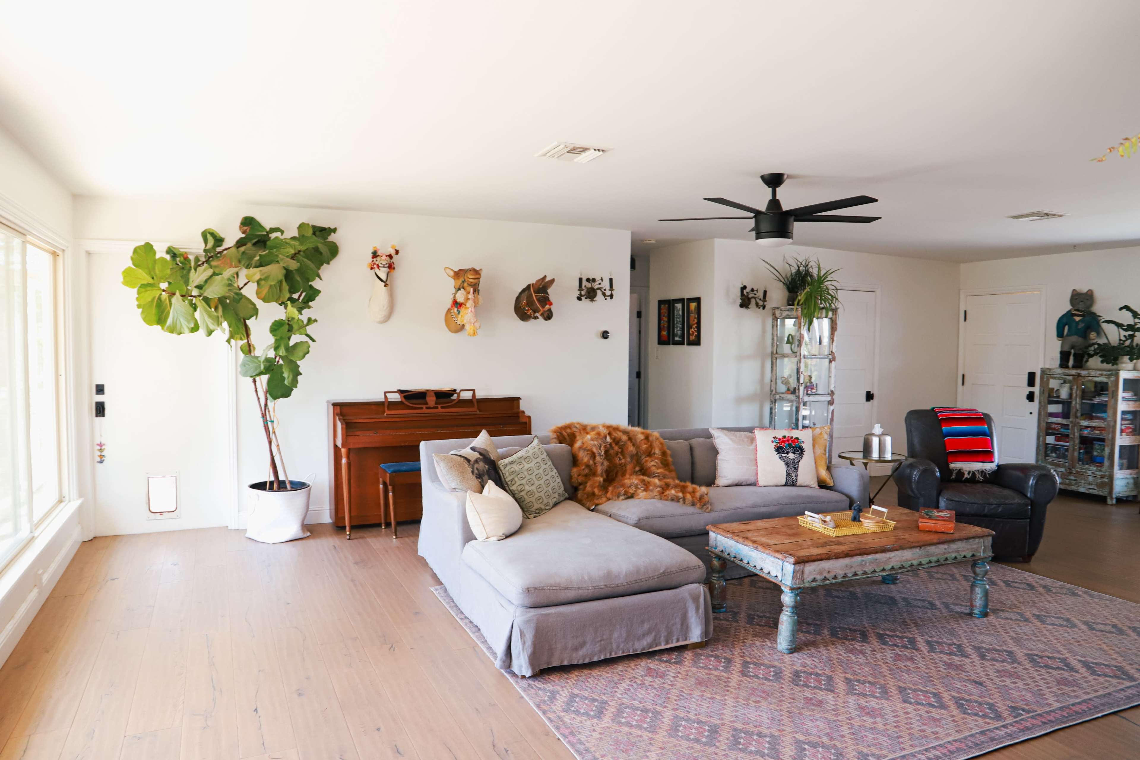 The image shows a spacious living room featuring a sectional sofa, a piano, plants, and decorative wall art.