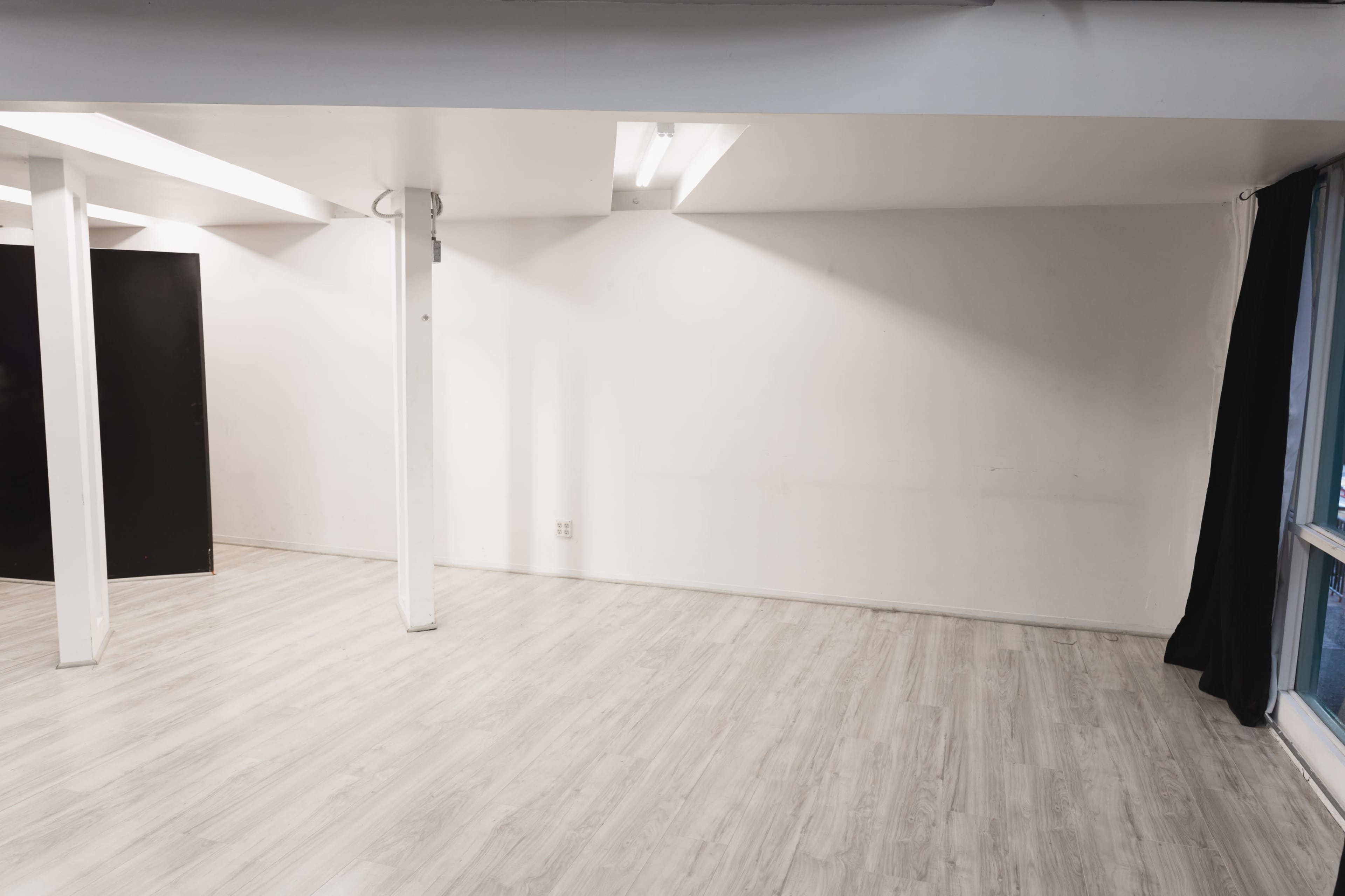 An empty room with polished light wooden flooring, white walls, and a black door on one side.