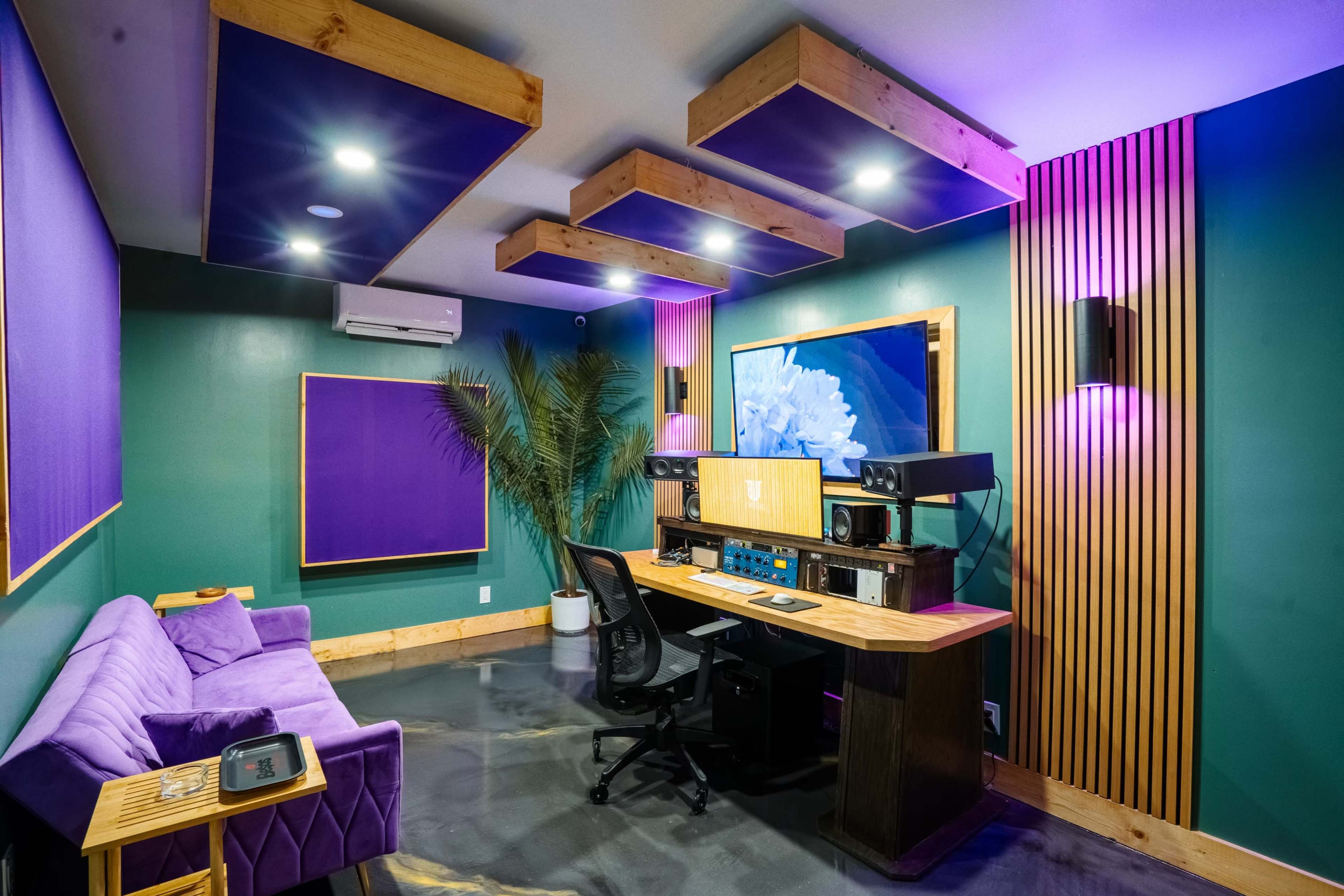 The image shows a modern recording studio with a purple and green color scheme, featuring a desk with audio equipment, a plush sofa, and decorative lighting.