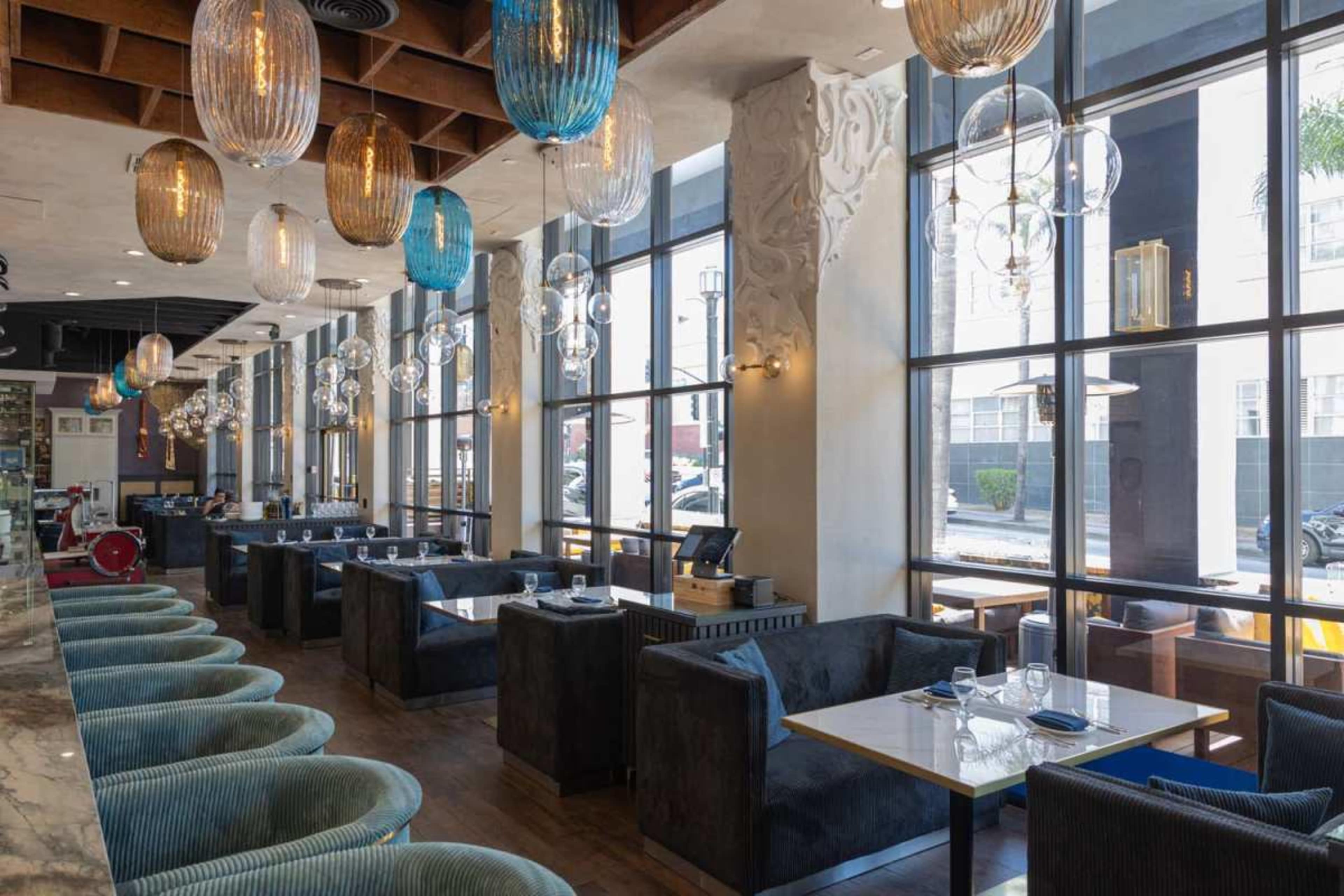 The image depicts a modern restaurant interior with spacious seating areas, large windows, and decorative pendant lights hanging from the ceiling.