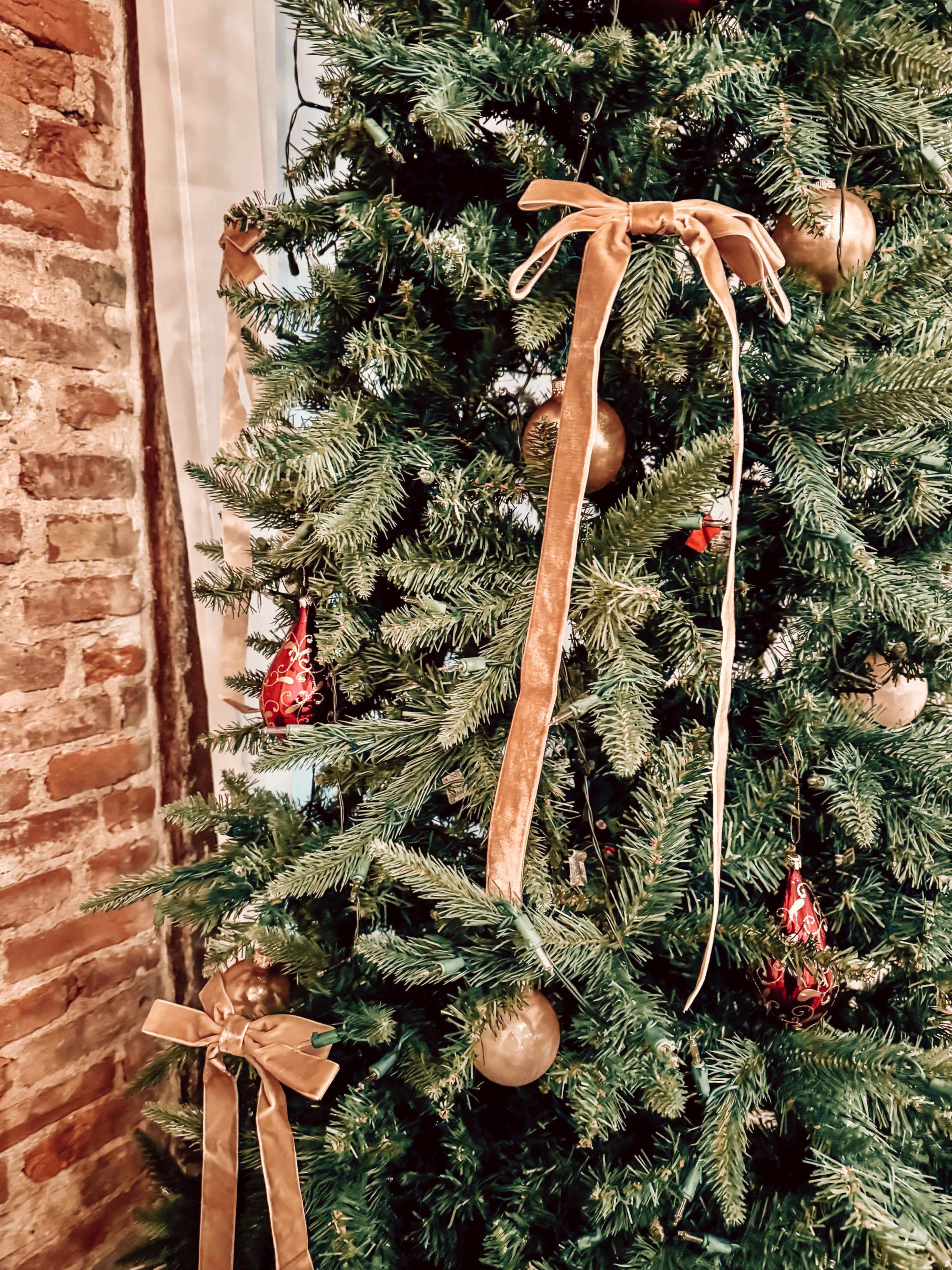 The image shows a decorated Christmas tree with velvet ribbons and ornaments, set against a brick wall backdrop.