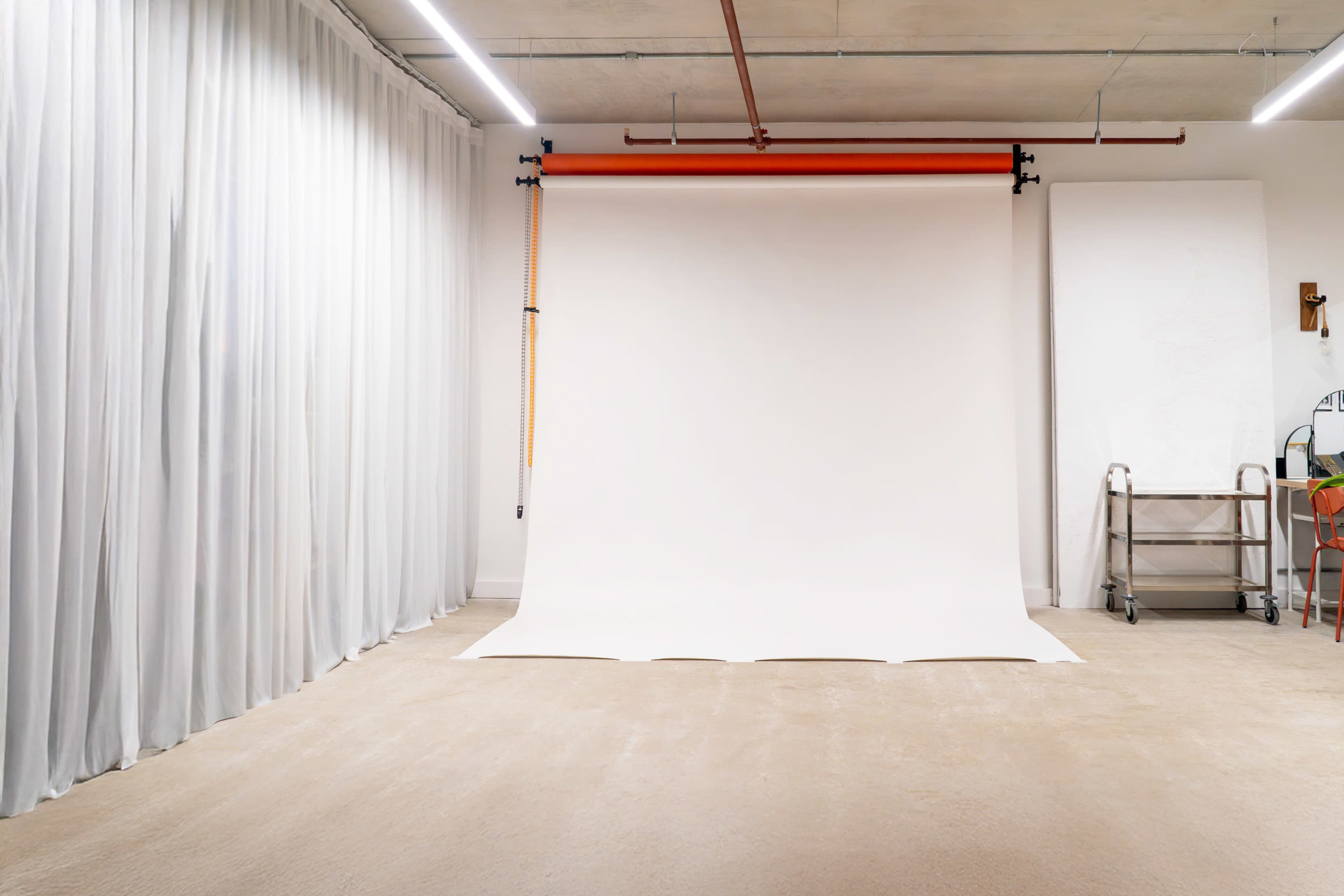 The image shows a photography studio with a white backdrop, beige carpet, and gray curtains on one side.