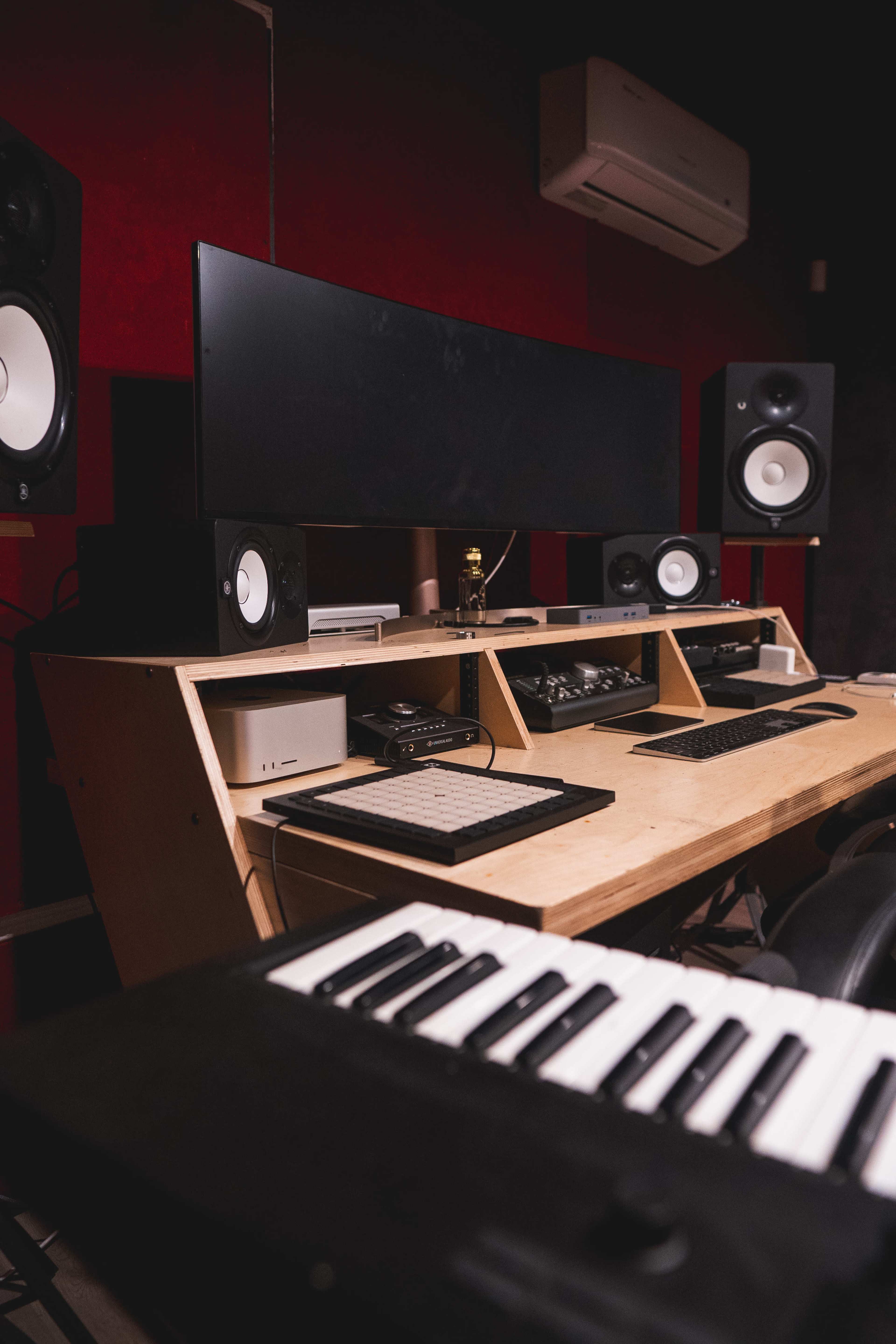 A music production studio setup with a large monitor, audio speakers, and a keyboard on a wooden desk.