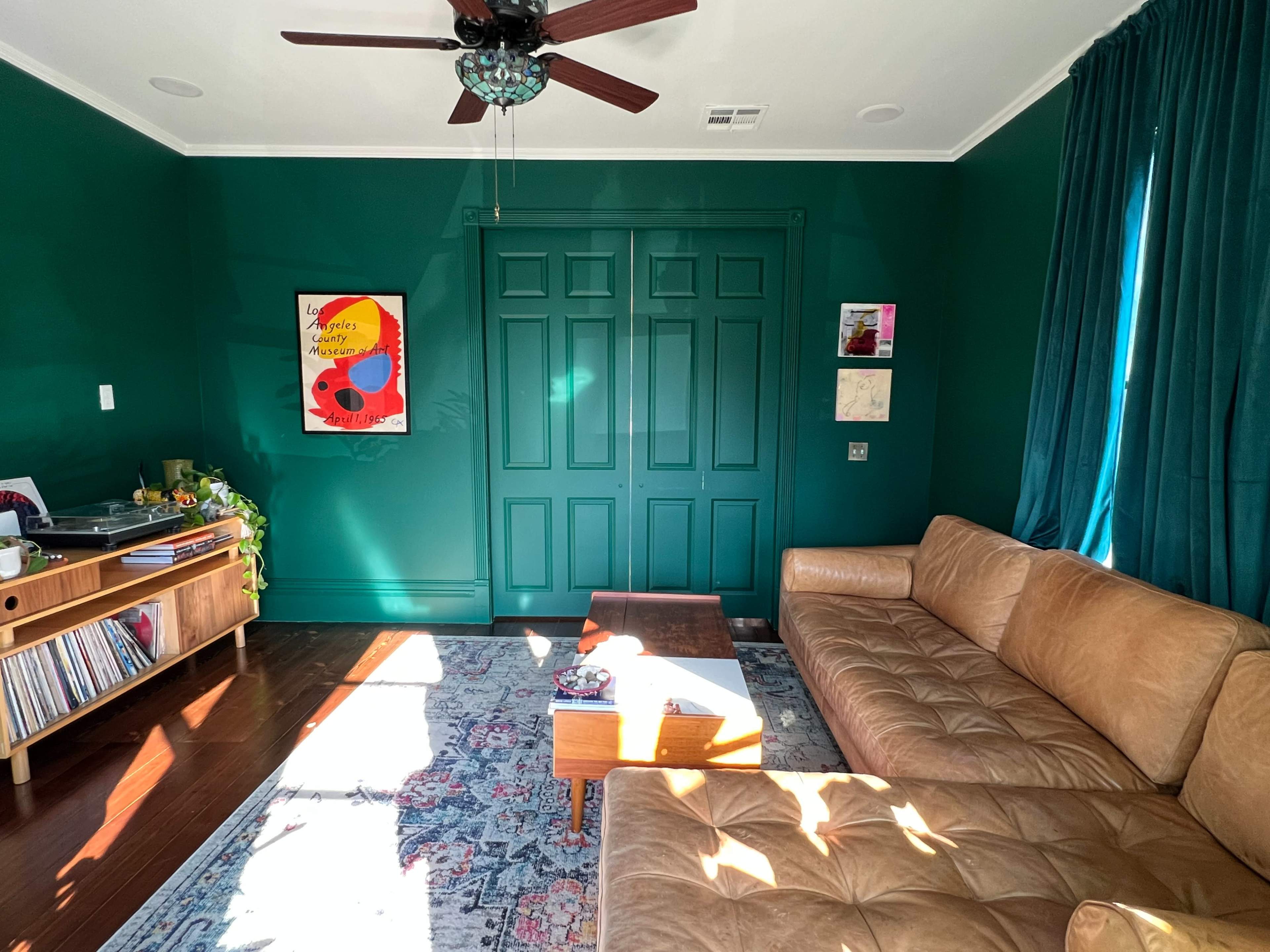 A living room with a green accent wall, a leather sofa, a wooden coffee table, and a record player next to a collection of vinyl records.