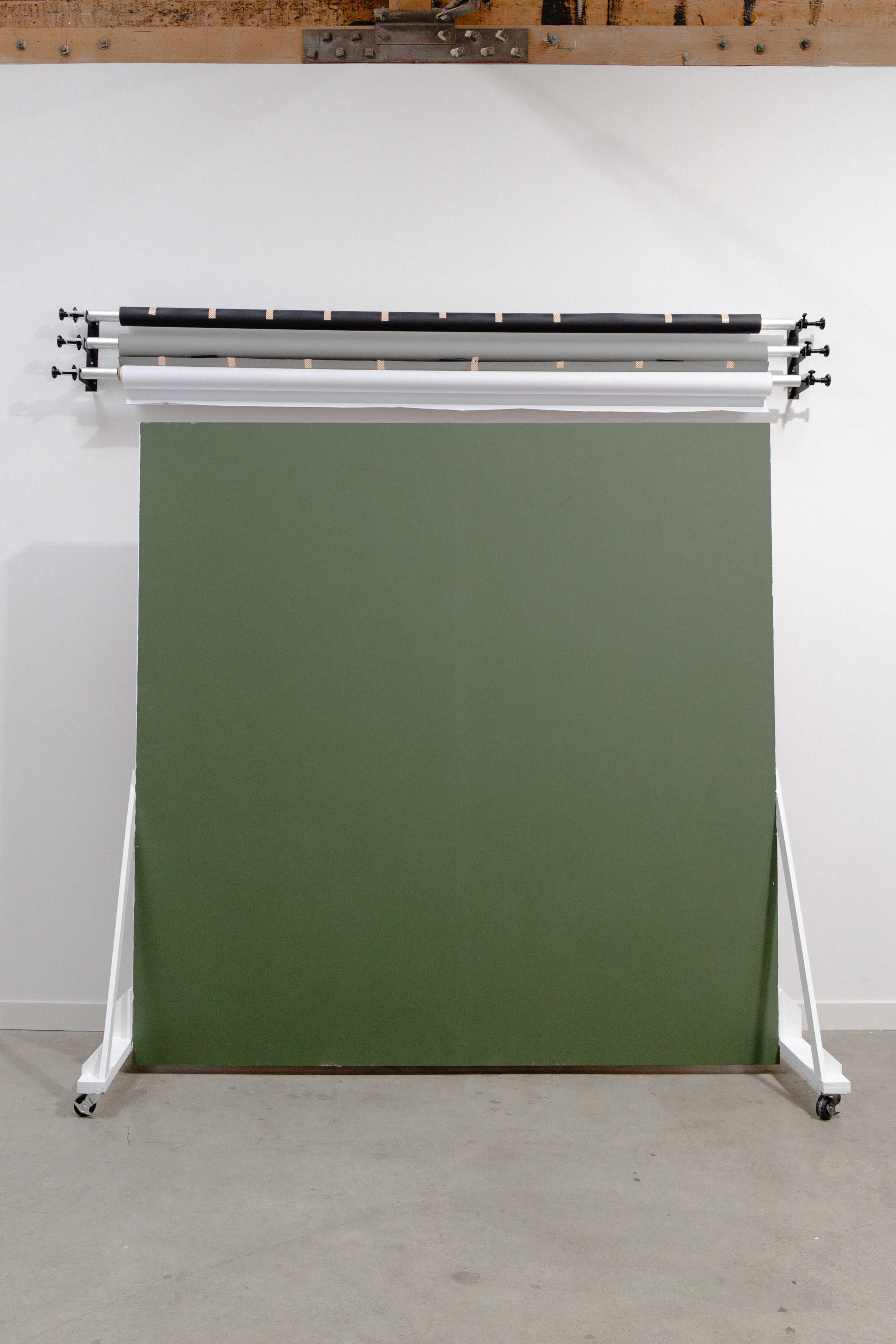 The image shows a green canvas backdrop mounted on a rolling frame with several support poles above it.
