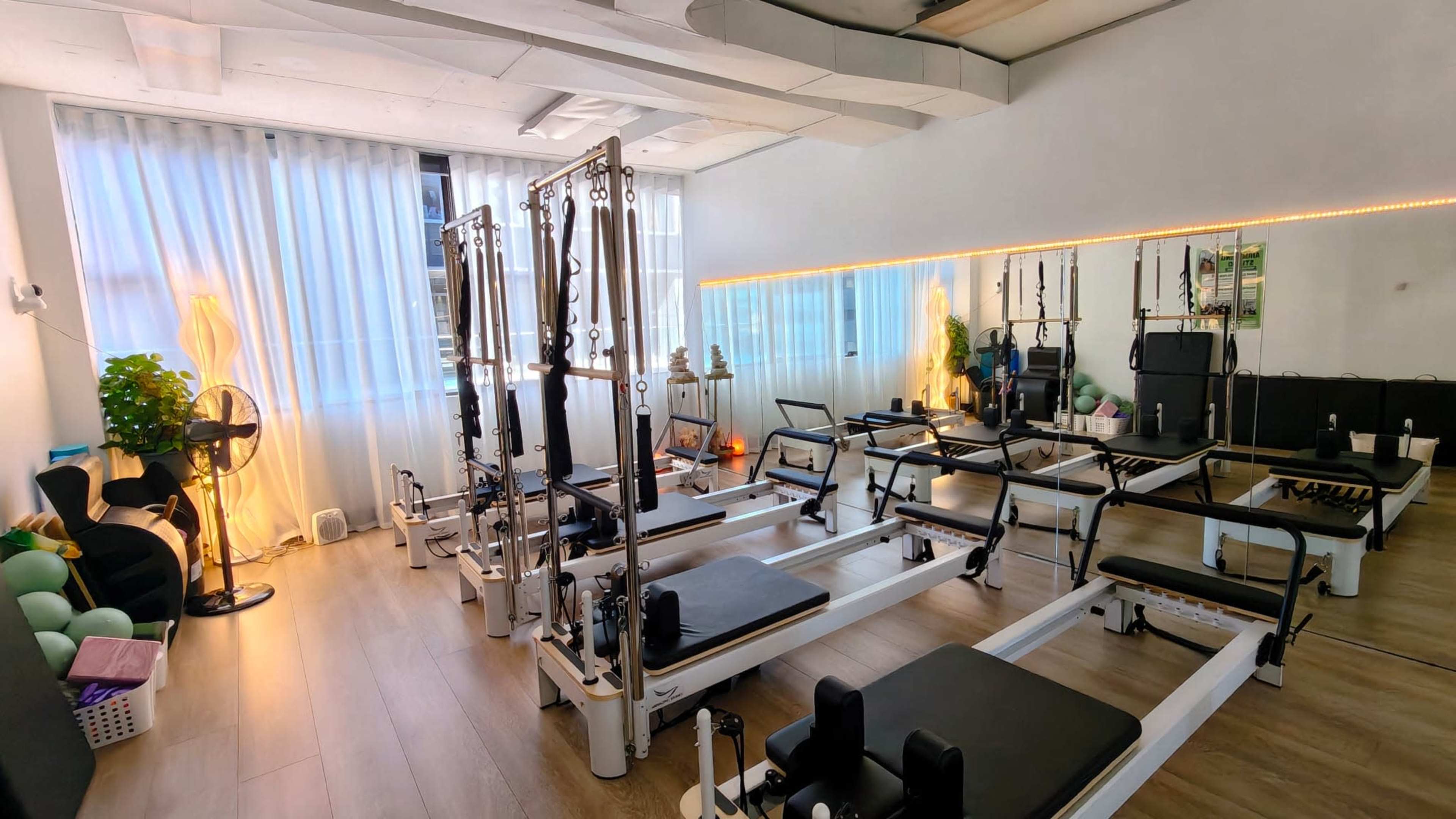 The image shows a well-lit Pilates studio with several reformer machines arranged in a spacious layout.
