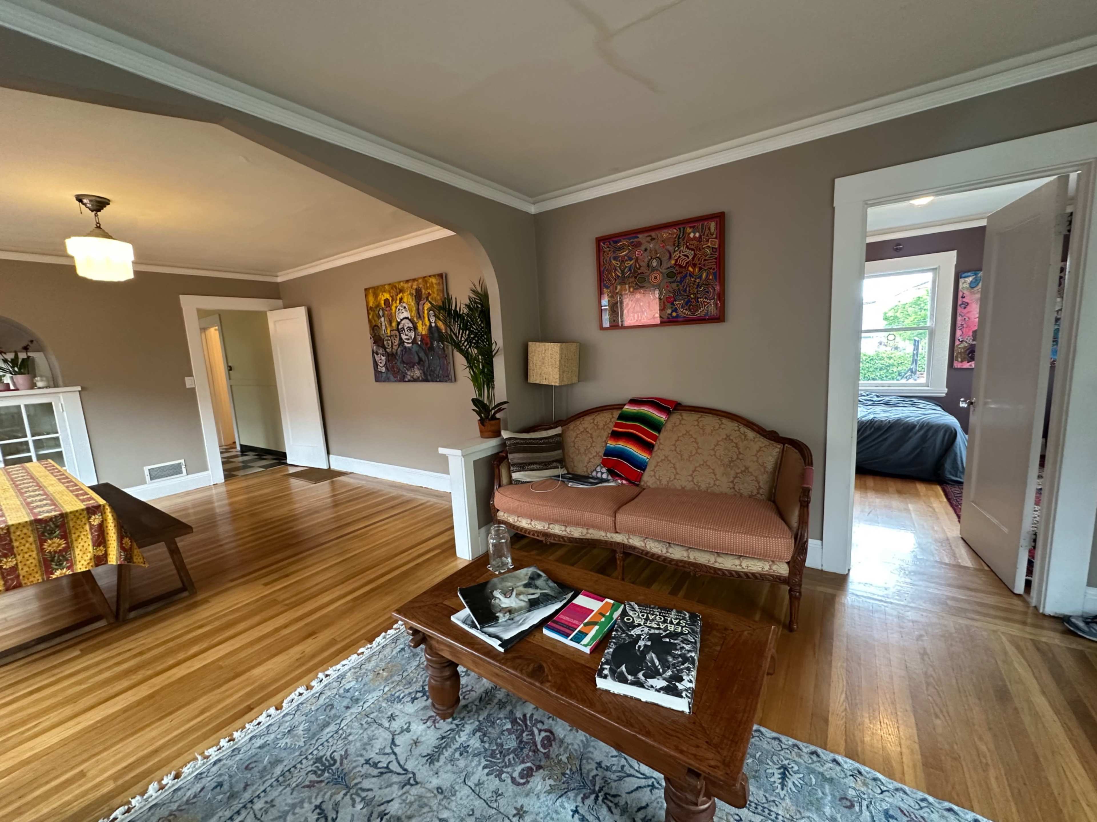 The image shows a living room area featuring a vintage sofa, a wooden coffee table with magazines, and a dining area in the background.