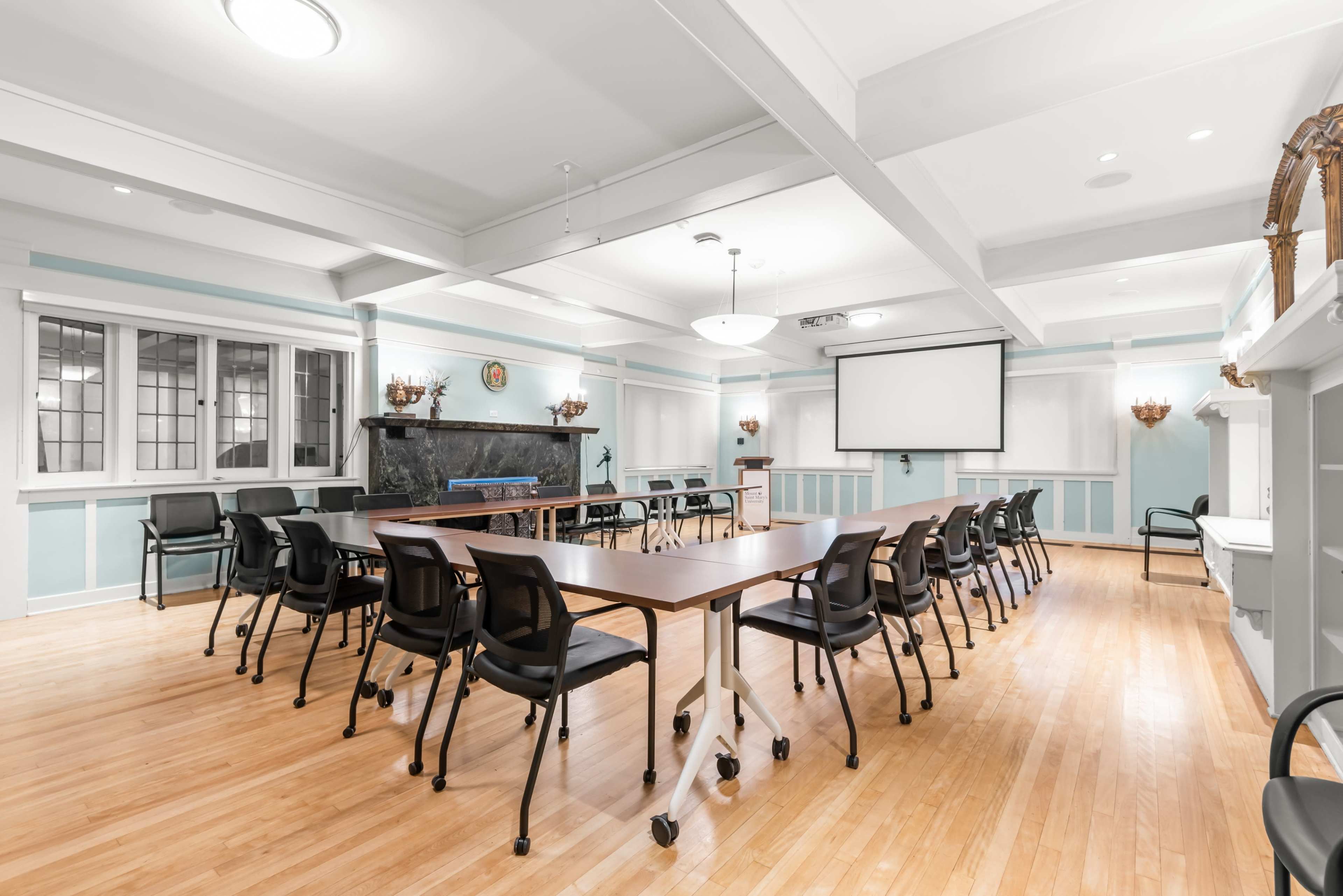The image shows a spacious meeting room with a long table set up in the center, surrounded by chairs, and equipped with a screen at one end.
