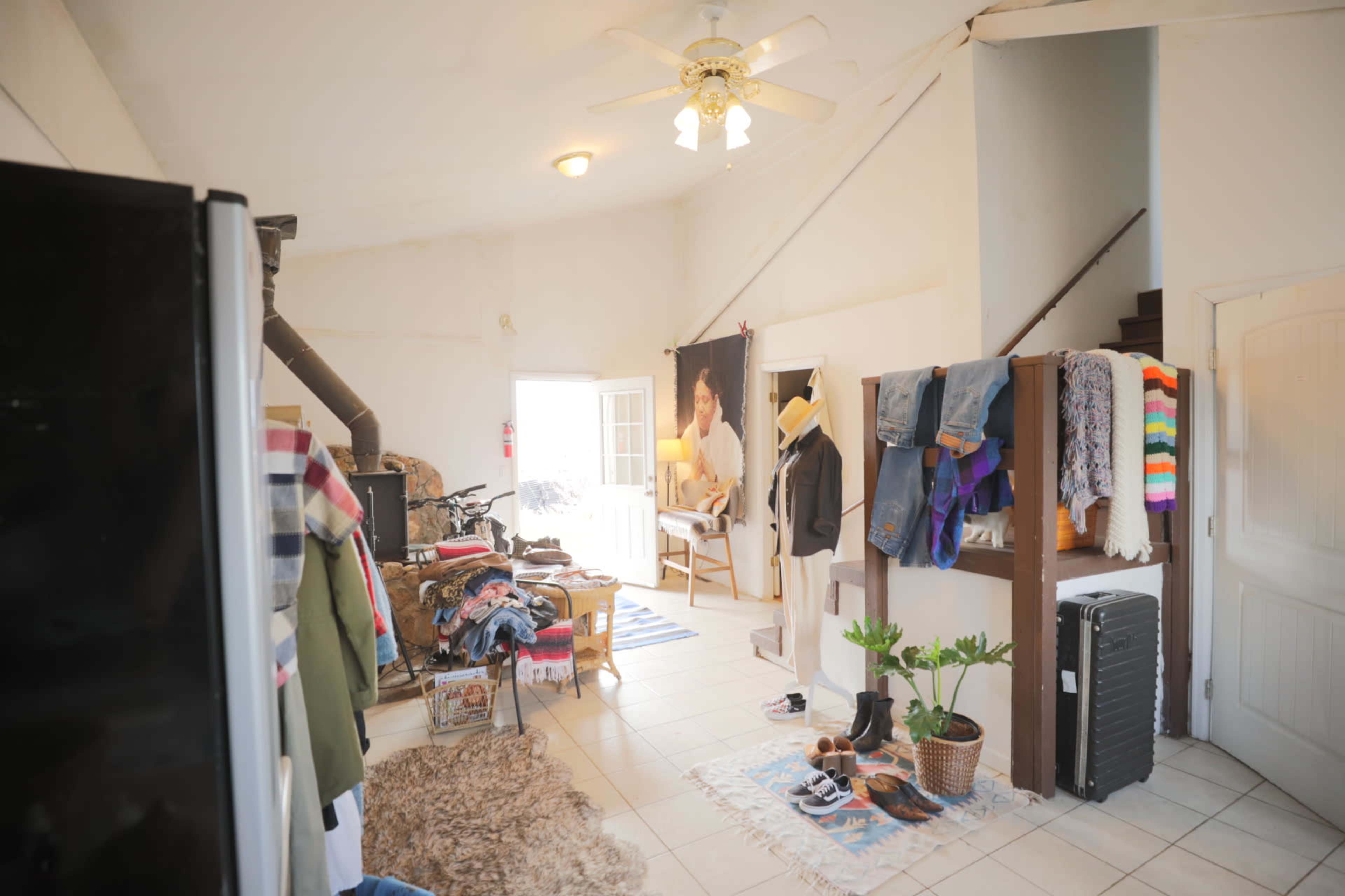 The image shows an open living space with clothing on racks, a small seating area, and a staircase leading to an upper level.