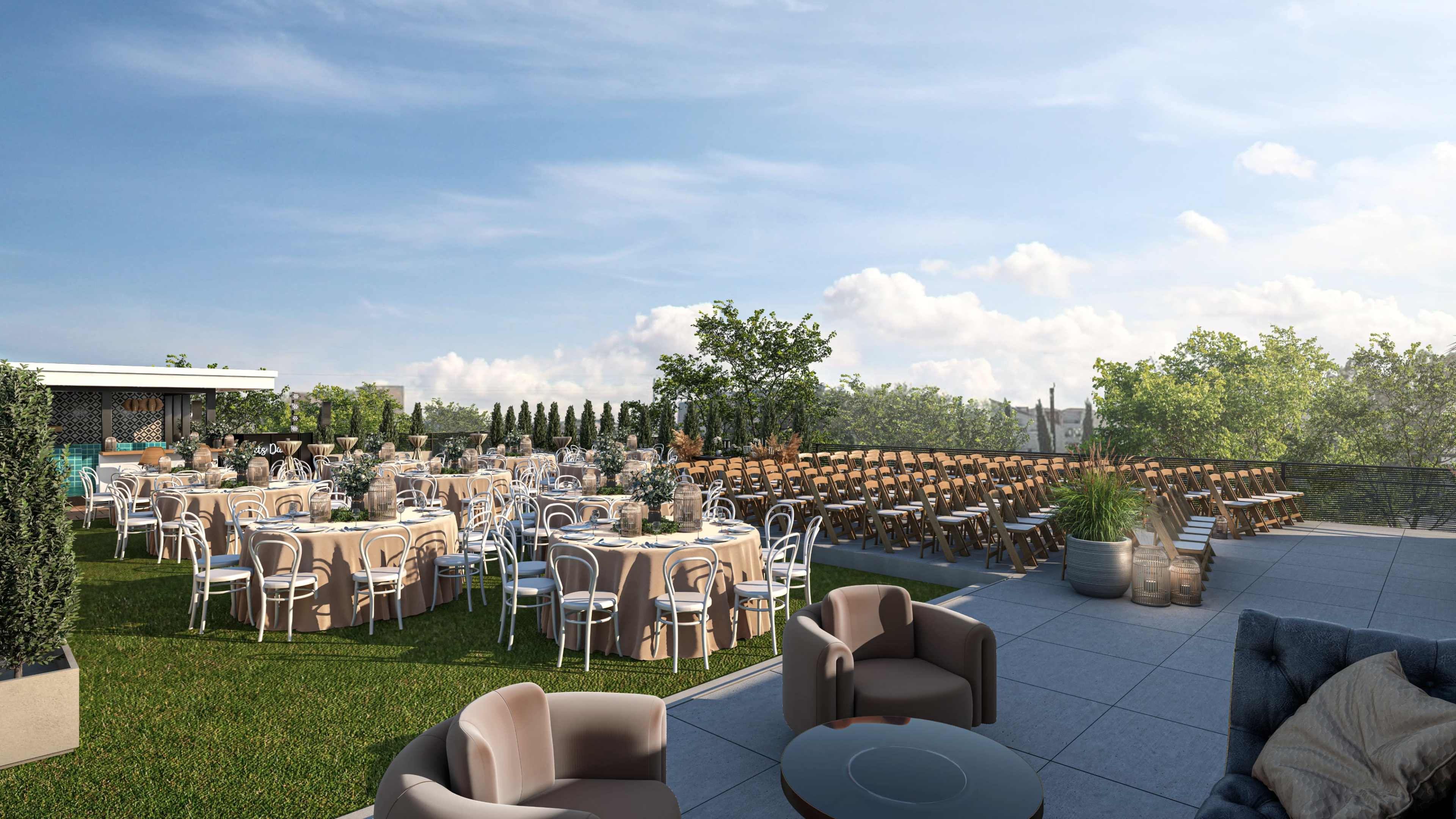 A rooftop venue is set up for an outdoor event, featuring round tables with beige tablecloths and rows of wooden chairs arranged on a grassy area amid greenery and a clear blue sky.