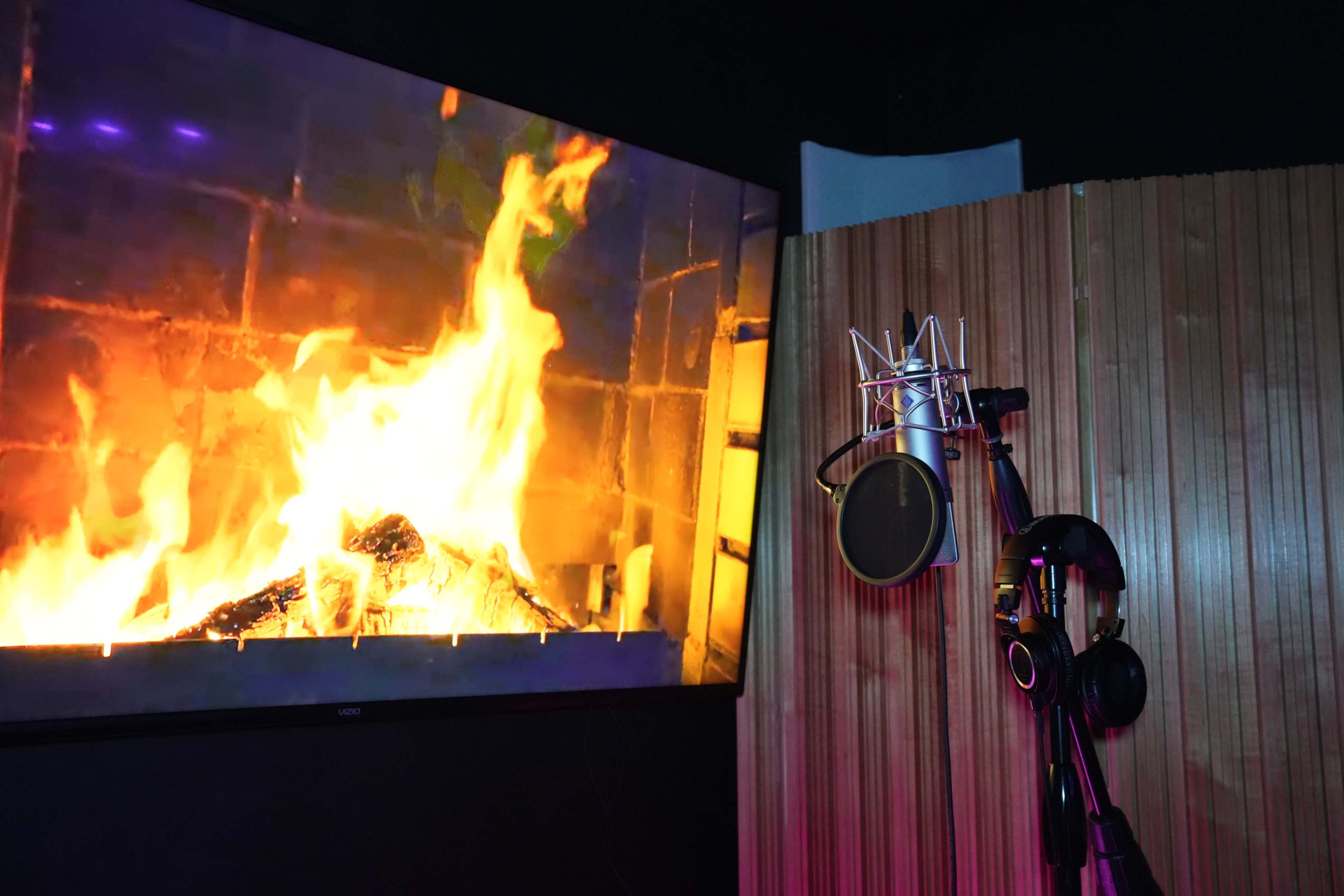 A studio room features a microphone and headphones beside a large screen displaying a burning fire.