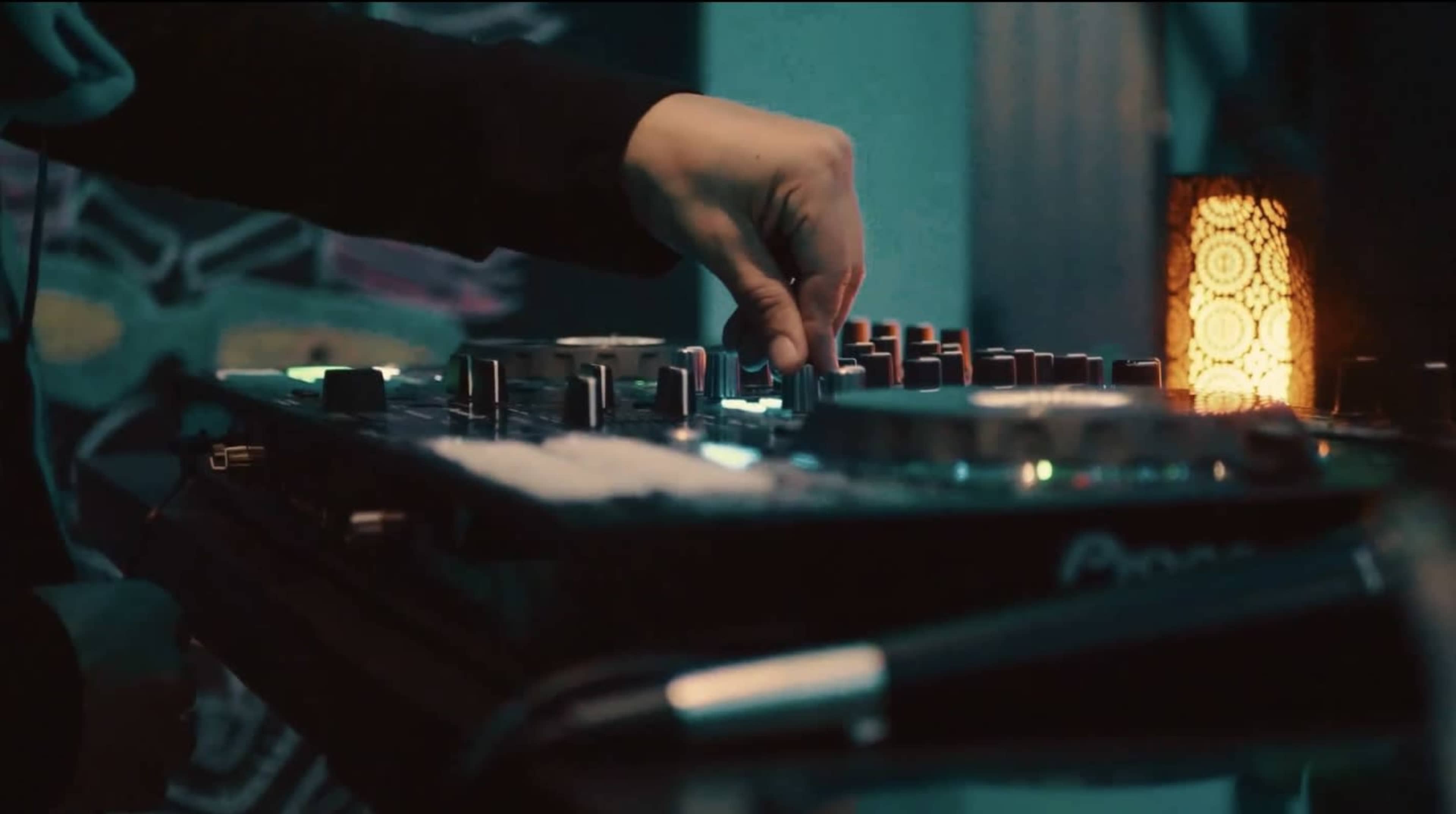 A hand adjusts the controls on a DJ mixer while a lamp emits a soft glow in the background.