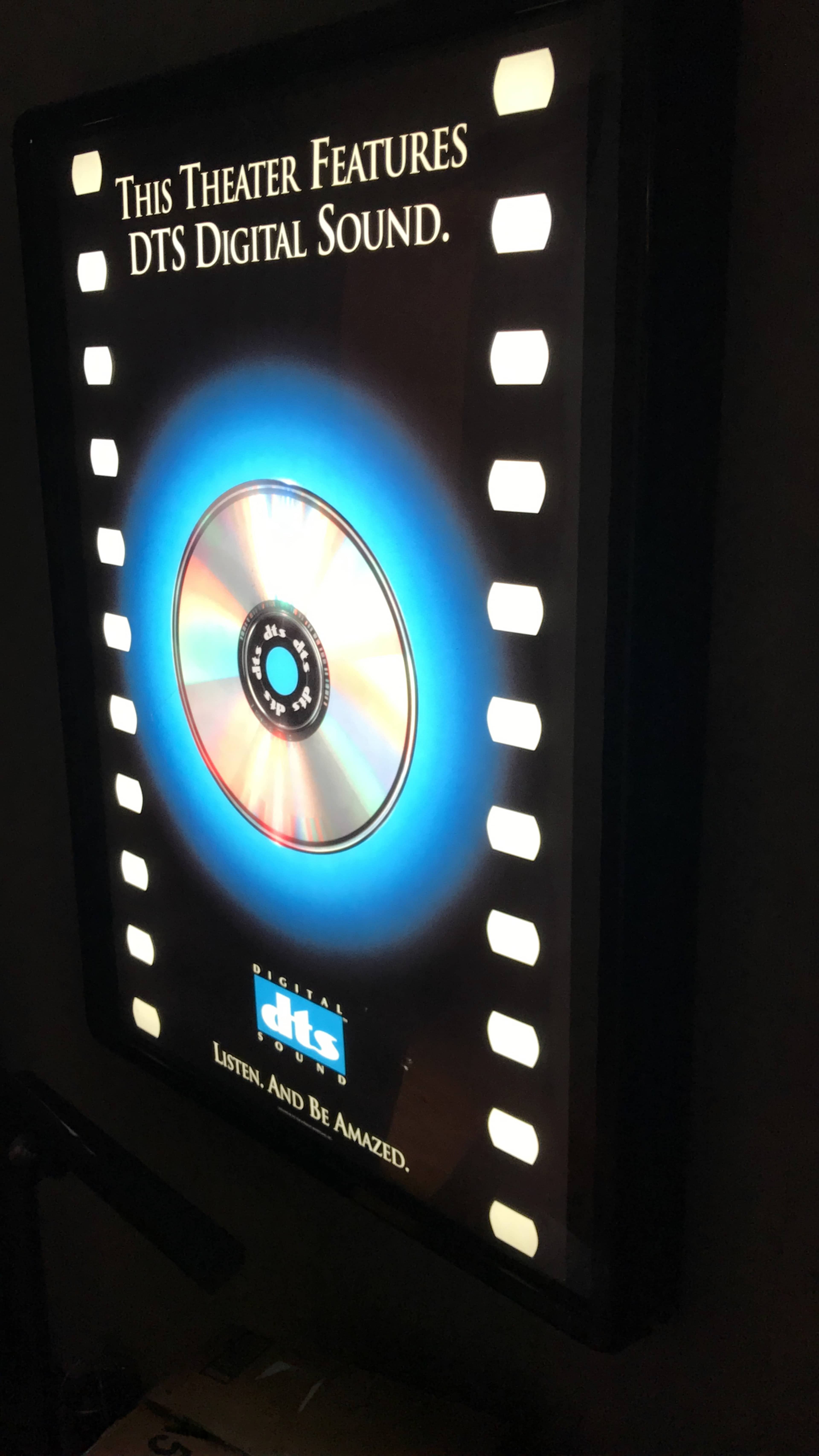 A lighted poster advertising a theater that features DTS digital sound, with a visual representation of a CD in the center.