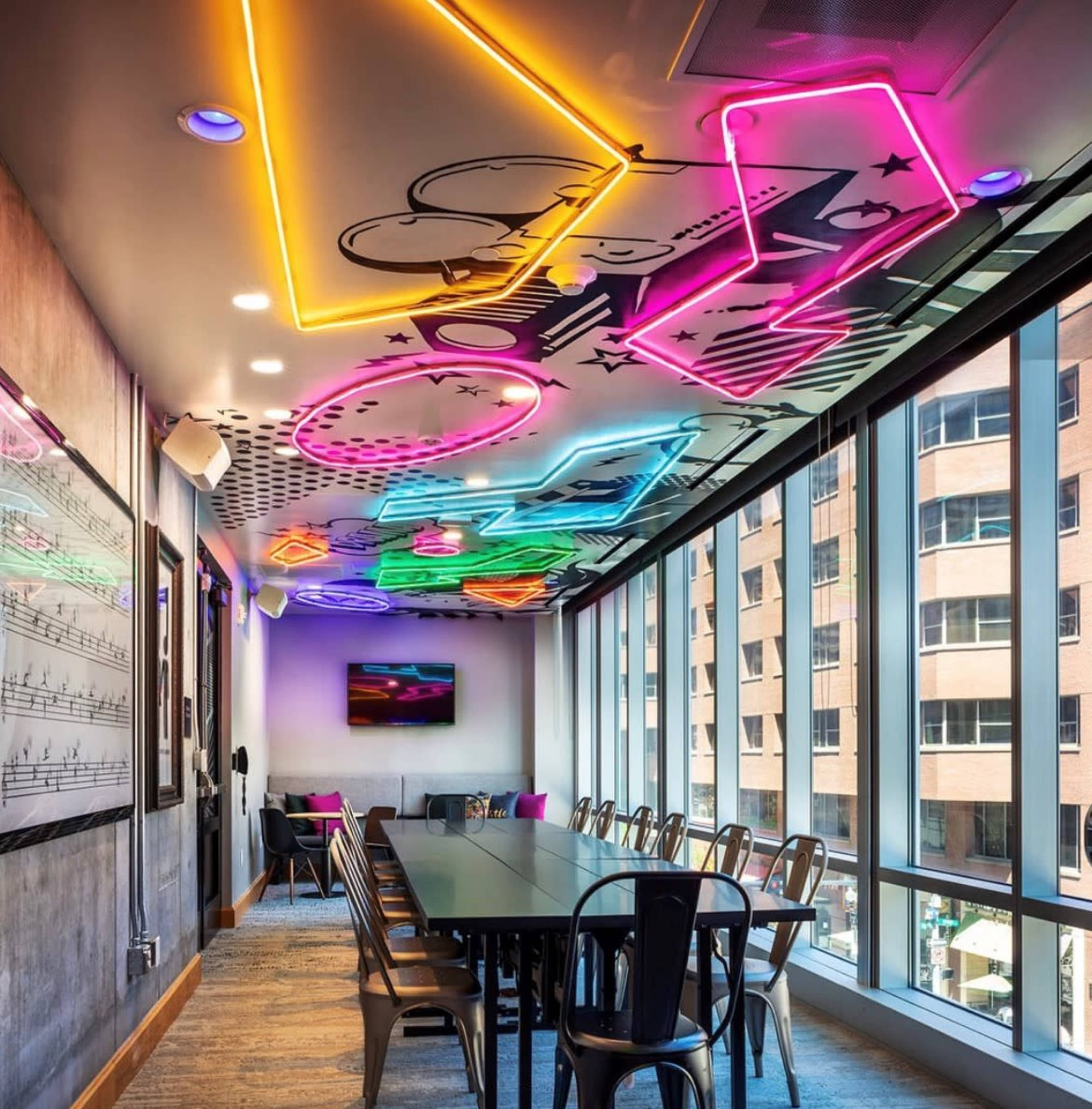 A modern conference room with a brightly lit ceiling featuring neon graphics and large windows overlooking a cityscape.