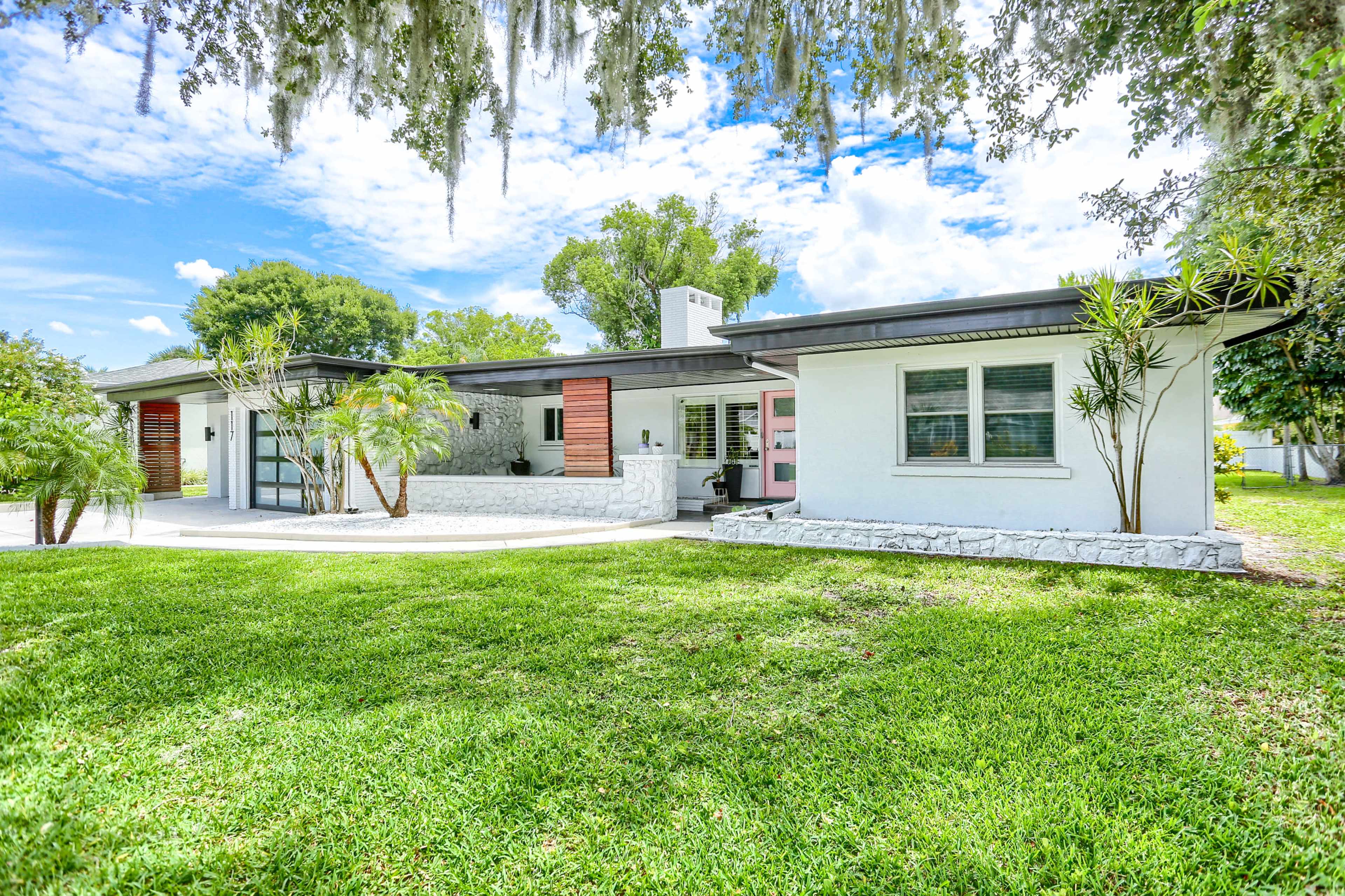 A modern single-story house with a well-maintained lawn features a mix of brick and stucco walls, large windows, and a prominent chimney.